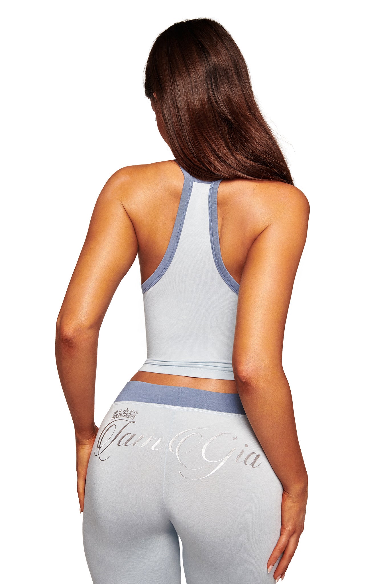 A woman with long brown hair wears the I.AM.GIA BLARE V-NECK TANK in two-tone powder blue and matching leggings, both form-fitting. Seen from the back, “Gian Gia” is inscribed in cursive on her leggings.