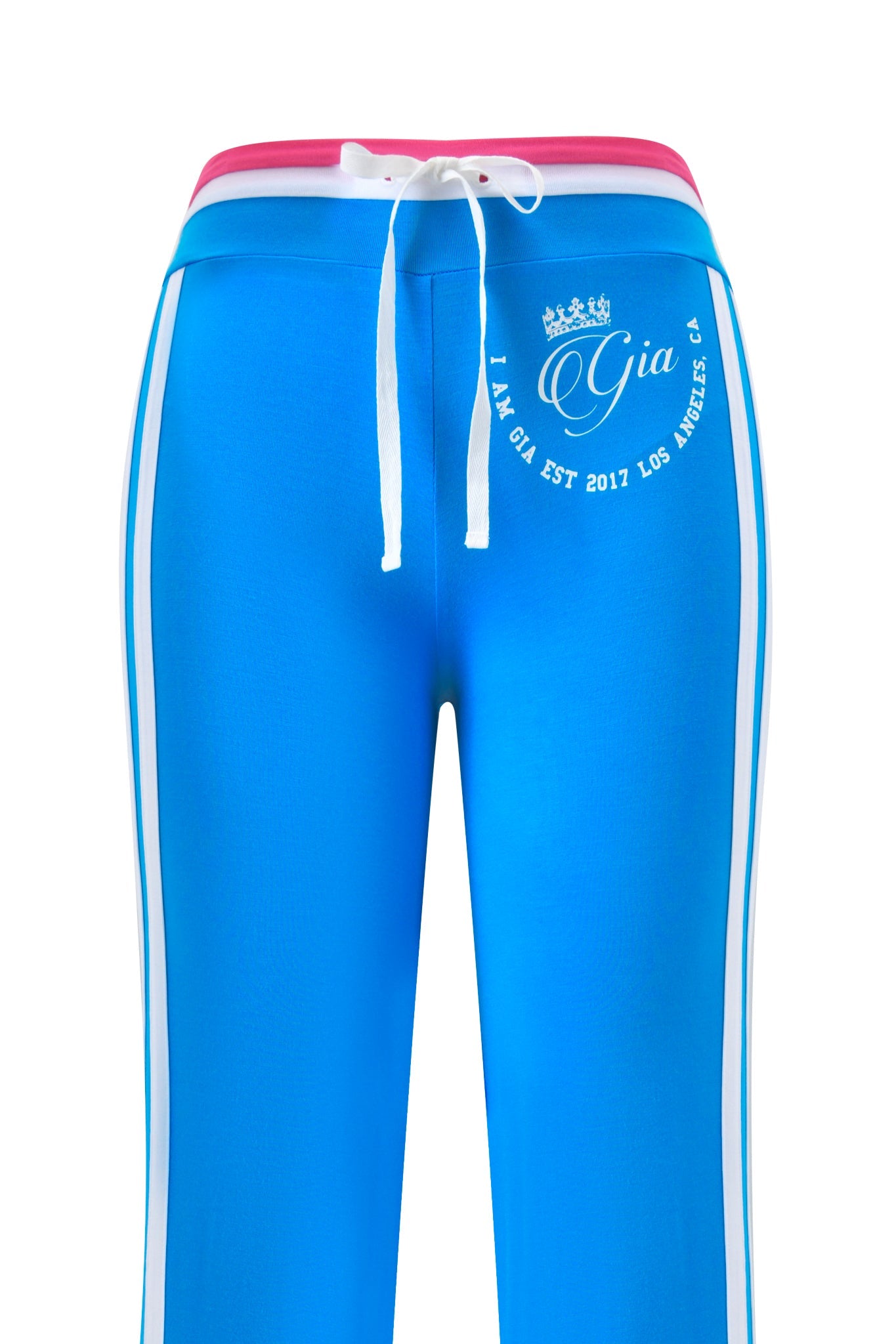 The BLARE STRIPED TRACKPANT by I.AM.GIA features a sky blue color with white side stripes, low-rise waist, pink waistband, white drawstring, and a front “Gia” logo with crown and “IAMGIA EST 2017 LOS ANGELES, CA” text.