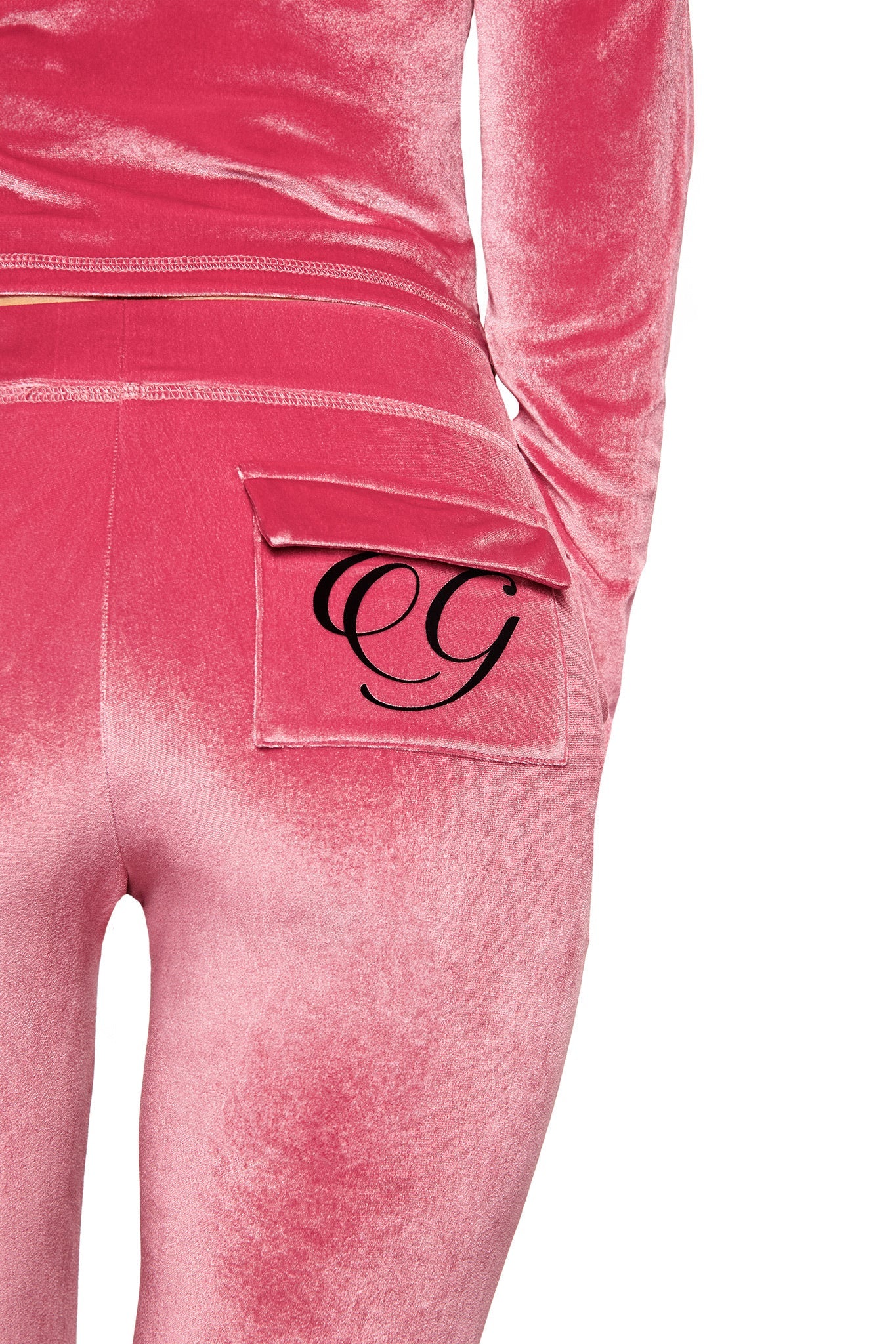 A person is seen from the back wearing the I.AM.GIA BLARE VELOUR POCKET TRACKPANT in pink, featuring a sculpted fit with a black “GG” monogram on the flap of the right back pocket.
