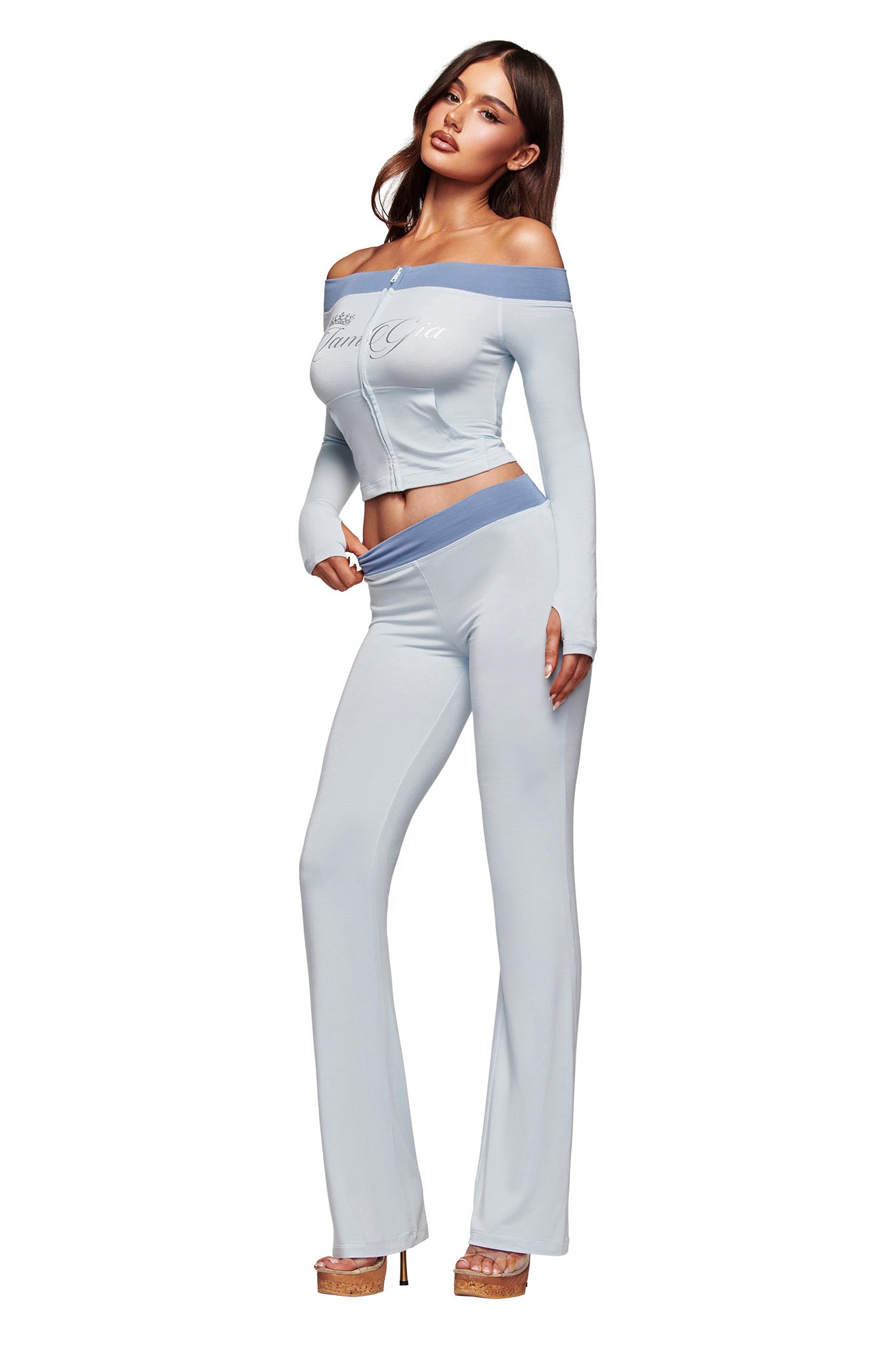 A woman poses against a white background in the I.AM.GIA BLARE OFF SHOULDER TOP - TWO TONE POWDER BLUE with matching high-waisted pants and platform heels, her long wavy hair flowing down.
