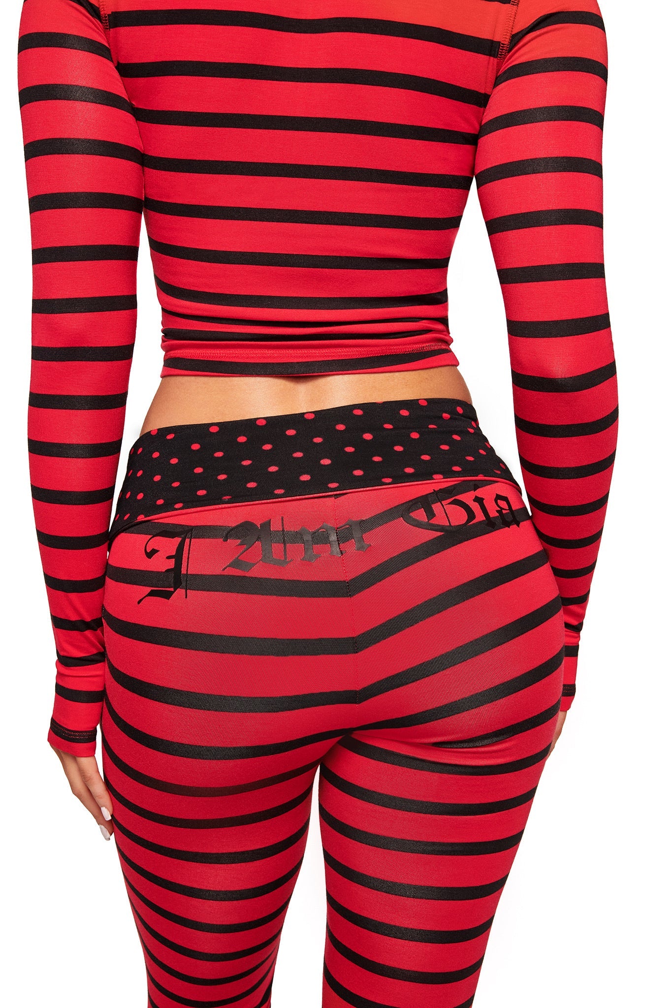 A person is shown from the back wearing the I.AM.GIA BLARE FOLDOVER TRACKPANT in red and black stripes, featuring a foldover waistband with black and red polka dots.