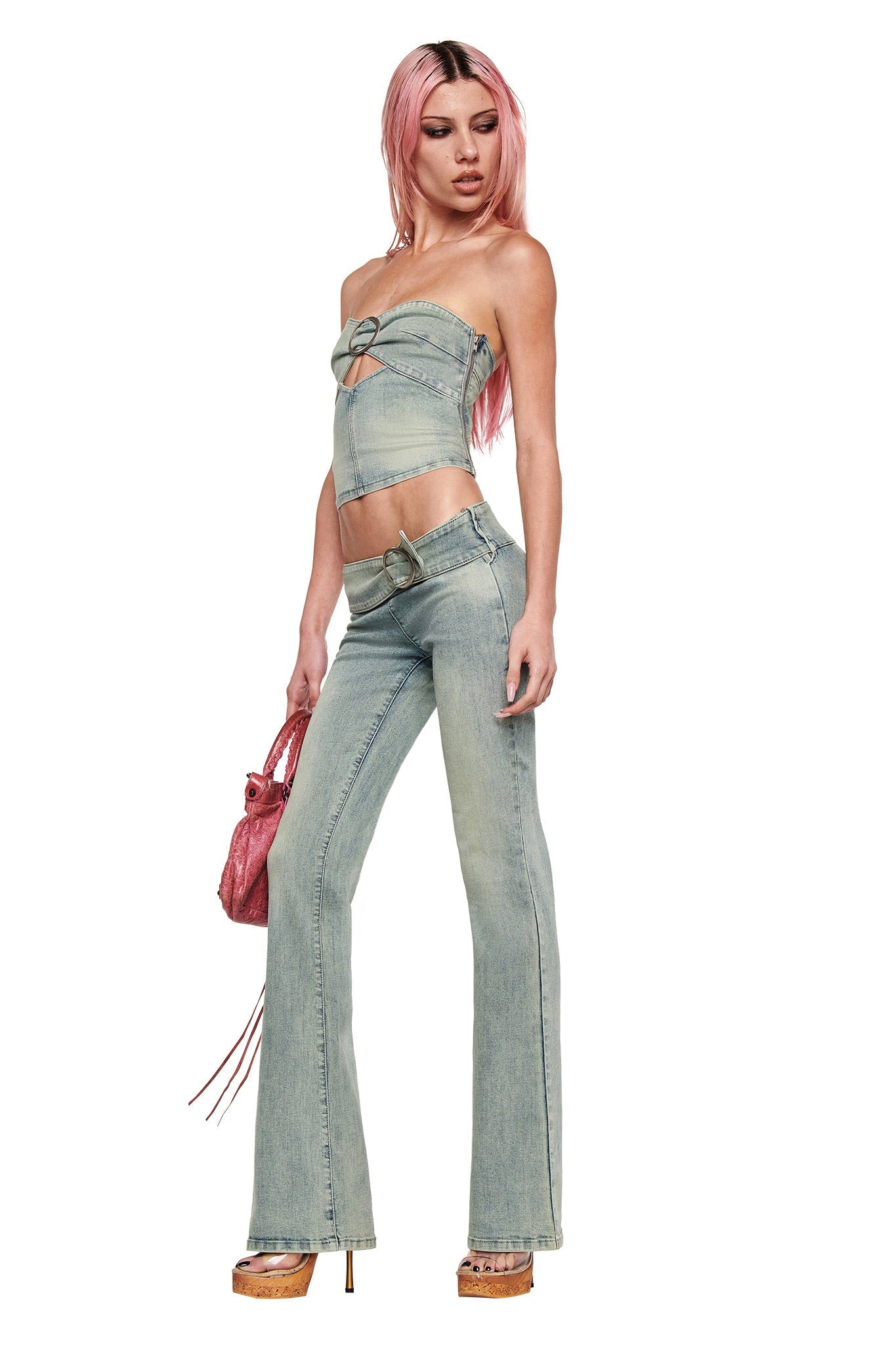 A woman with long pink hair poses confidently against a white background, wearing the I.AM.GIA JENN DENIM BOOB TUBE in blue with matching high-waisted flare jeans, a small pink bag, and wooden platform heels.