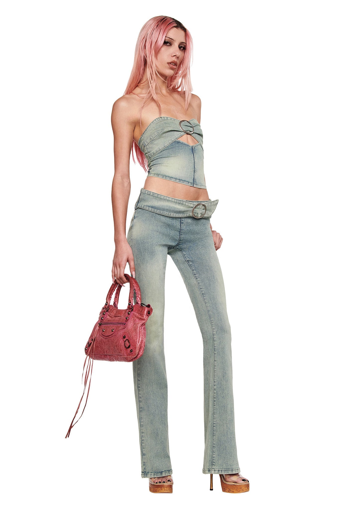 A person with long pink hair wears the I.AM.GIA JENN JEAN - BLUE, styled with a denim strapless top, statement belt buckle, pink handbag, and platform heels.