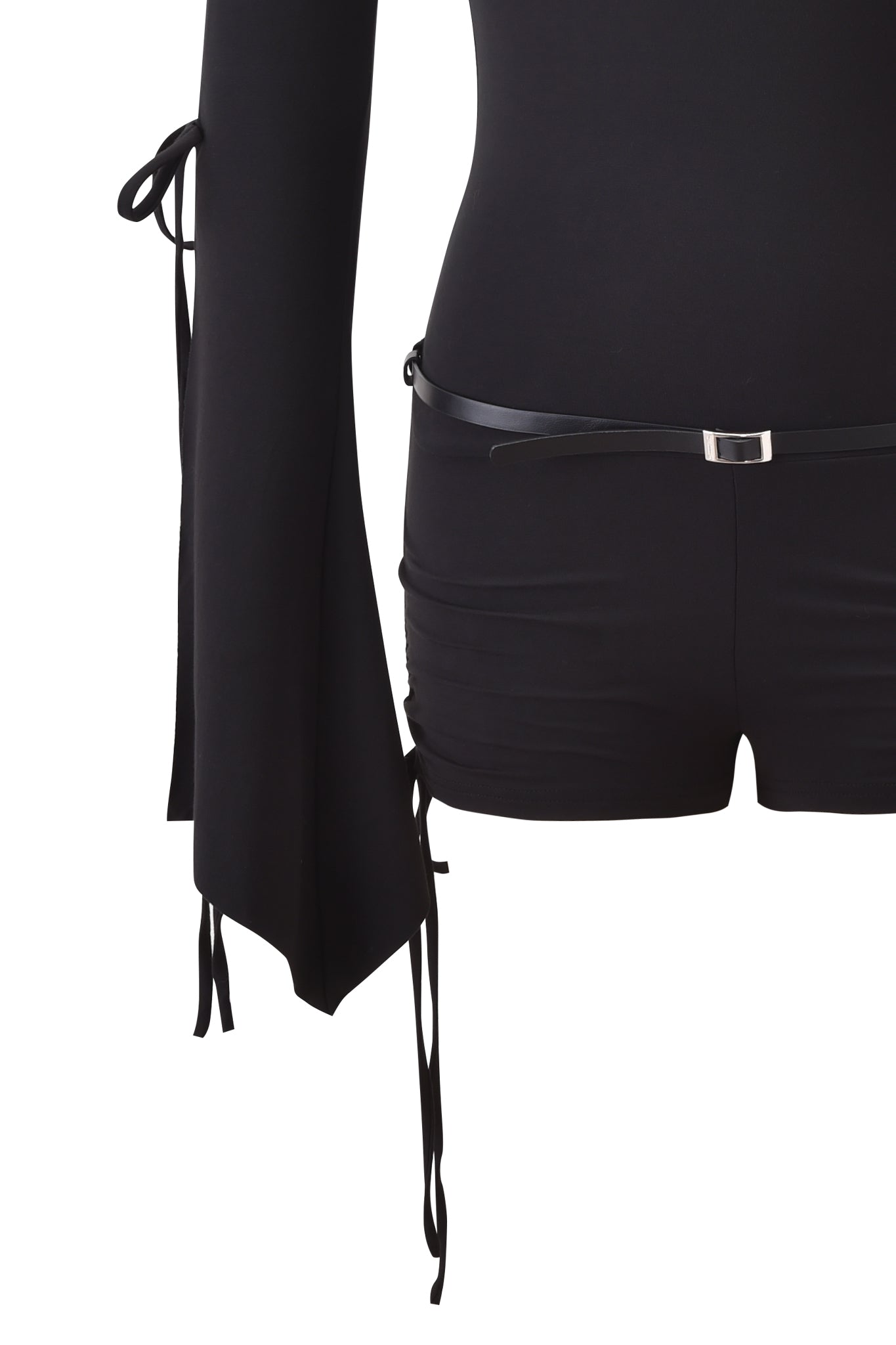 A close-up shot of a person wearing the SAPHY PLAYSUIT - BLACK by I.AM.GIA, showcasing its long sleeves with ribbon ties, fitted bodycon shorts, and a sleek thin black belt. The image is cropped at the chest and upper thighs.