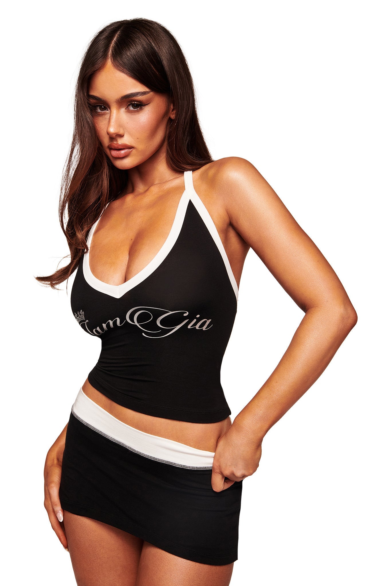 A woman wears the I.AM.GIA BLARE V-NECK TANK in black and white, styled with a fitted black mini skirt featuring a white waistband, as she poses against a white background.