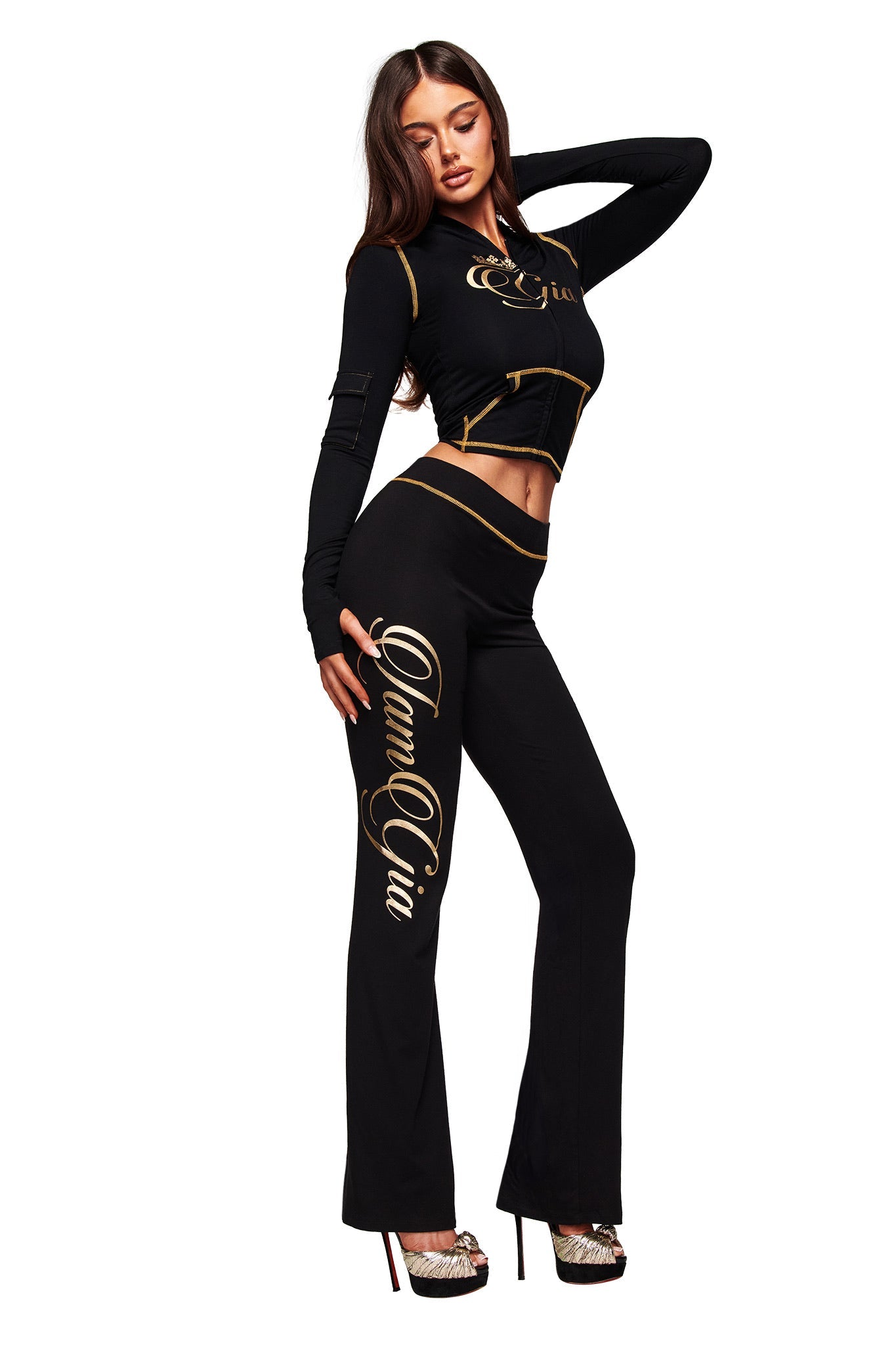 A woman wears the I.AM.GIA BLARE FORM TRACKPANT in black and gold, featuring a striking metallic print.