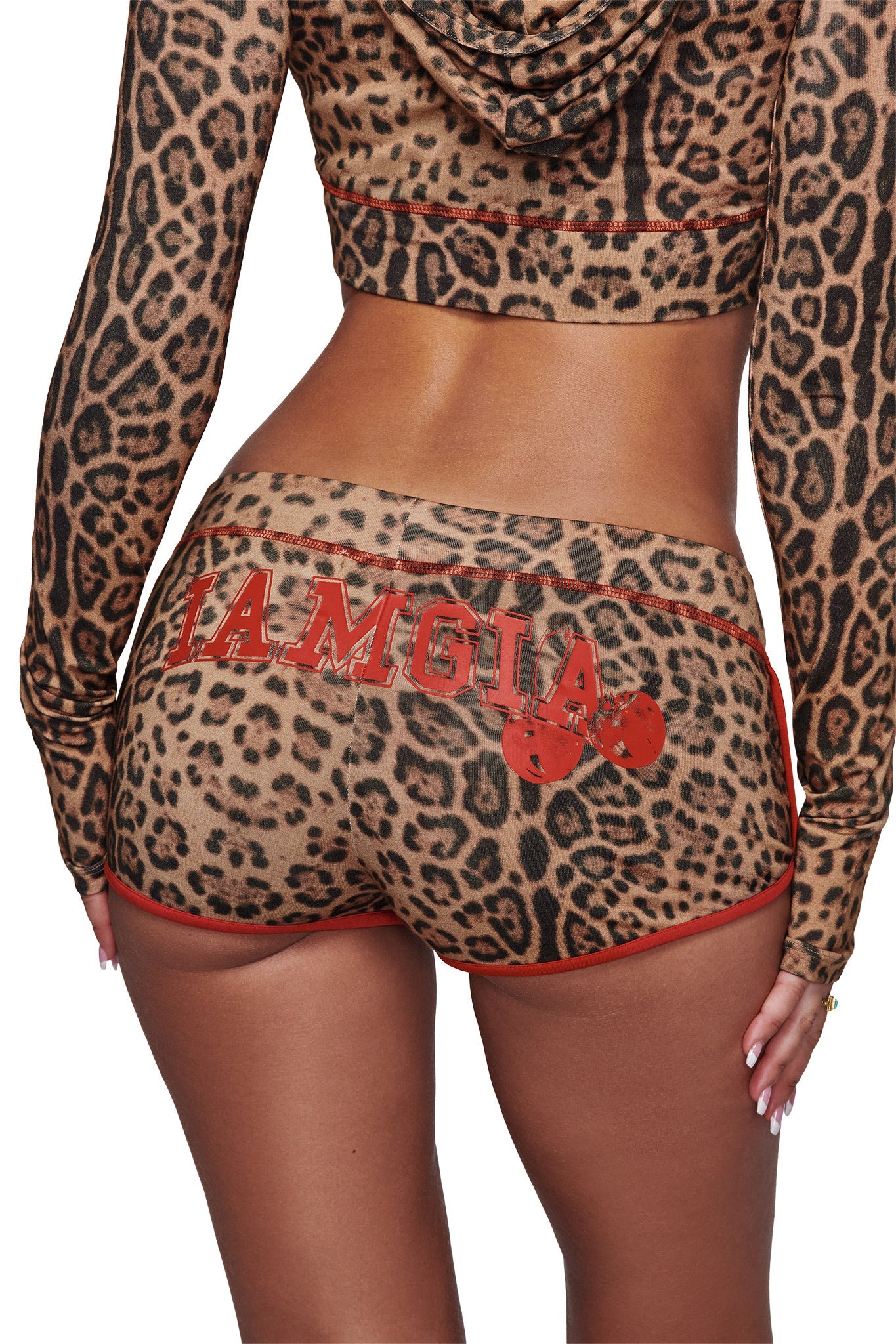 A person is wearing the I.AM.GIA BLARE DOLPHIN SHORT - PANTHERA, featuring a leopard print with red trim, styled for summer adventures and paired with a matching hoodie adorned with "I.AM.GIA" and two red boxing gloves on the back.