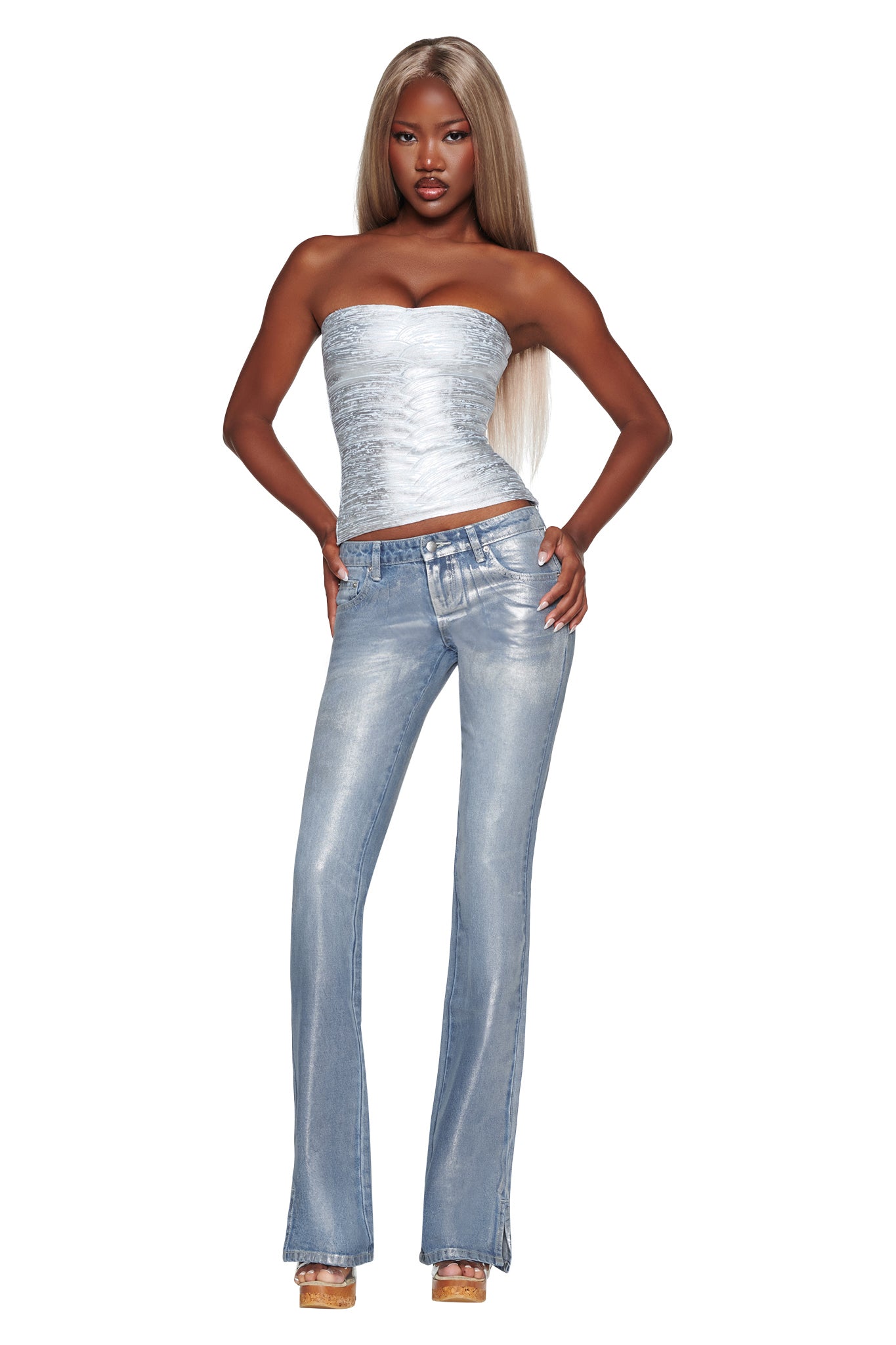 Woman with long blonde hair wearing the I.AM.GIA RENATA JEAN in Silver Metallic Wash, styled with a strapless silver top and platform heels, standing with hands on hips against a white background.