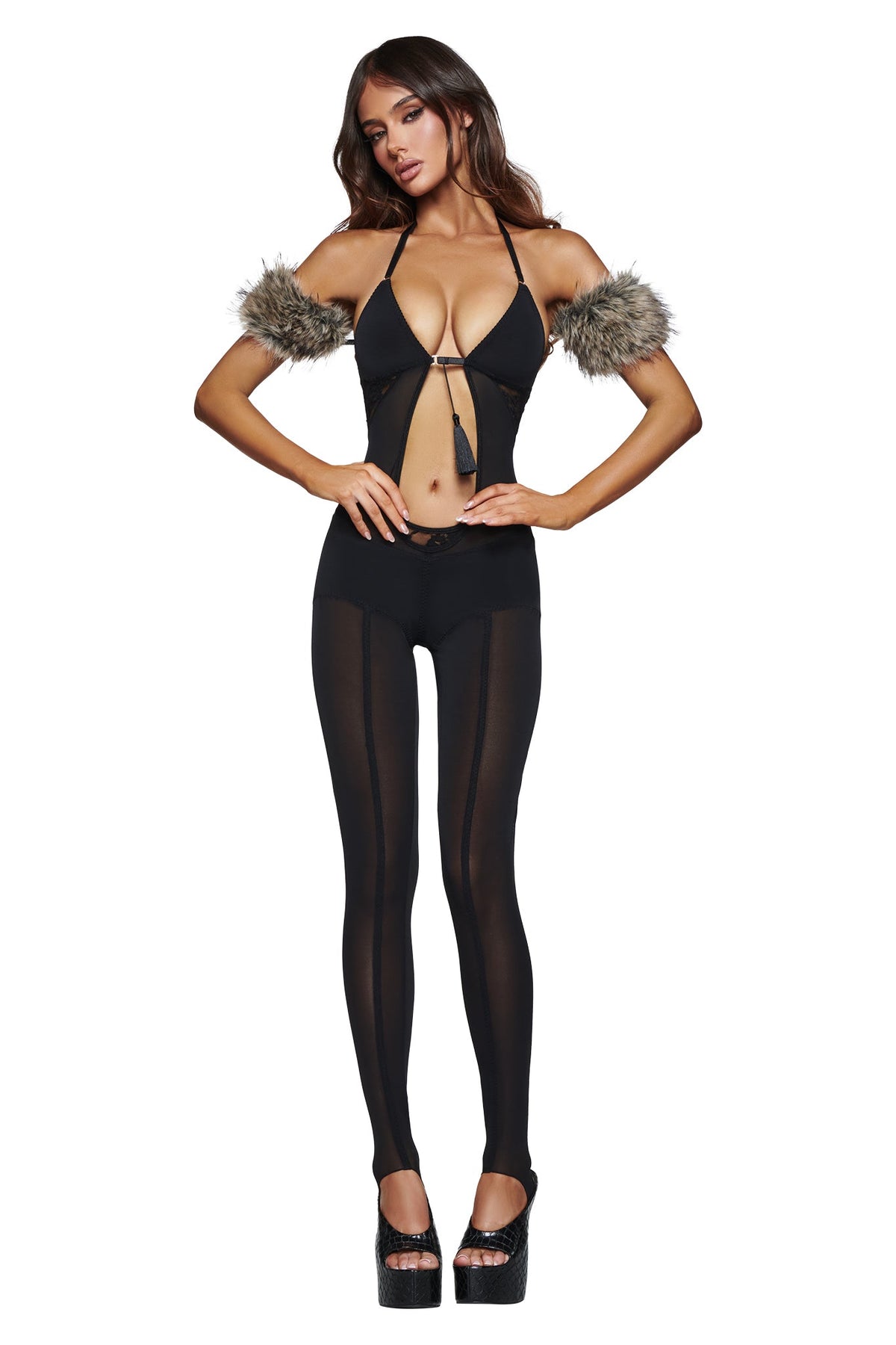 A woman poses against a white background wearing the AZARI CATSUIT - BLACK by I.AM.GIA, featuring sheer mesh leggings, faux fur arm cuffs, and black platform heels—a striking ensemble perfect for making a bold Halloween statement.