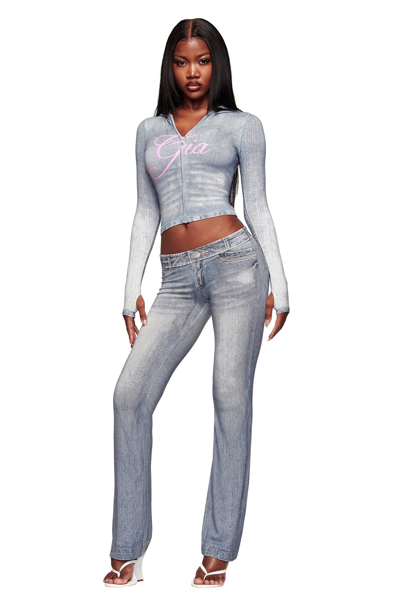 A woman stands confidently in the I.AM.GIA BLARE HOODIE - DENIM TROMPE L'OEIL, paired with matching jeans and white heeled sandals. Her long, straight hair completes the look.