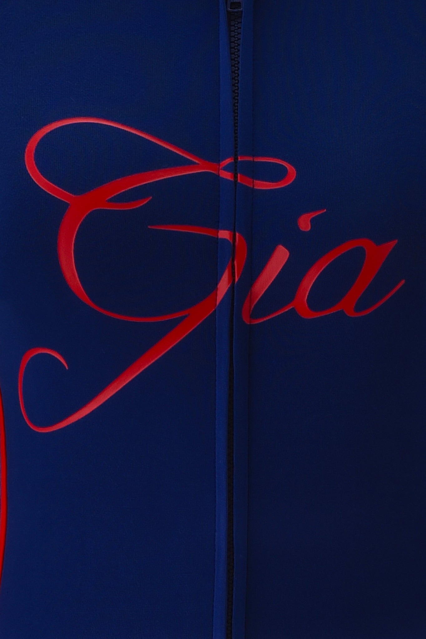 Close-up of the buttery-soft BLARE SPORT HOODIE AND HEADBAND in navy by I.AM.GIA, featuring "Gia" in large red script and a black zipper running vertically down the center.