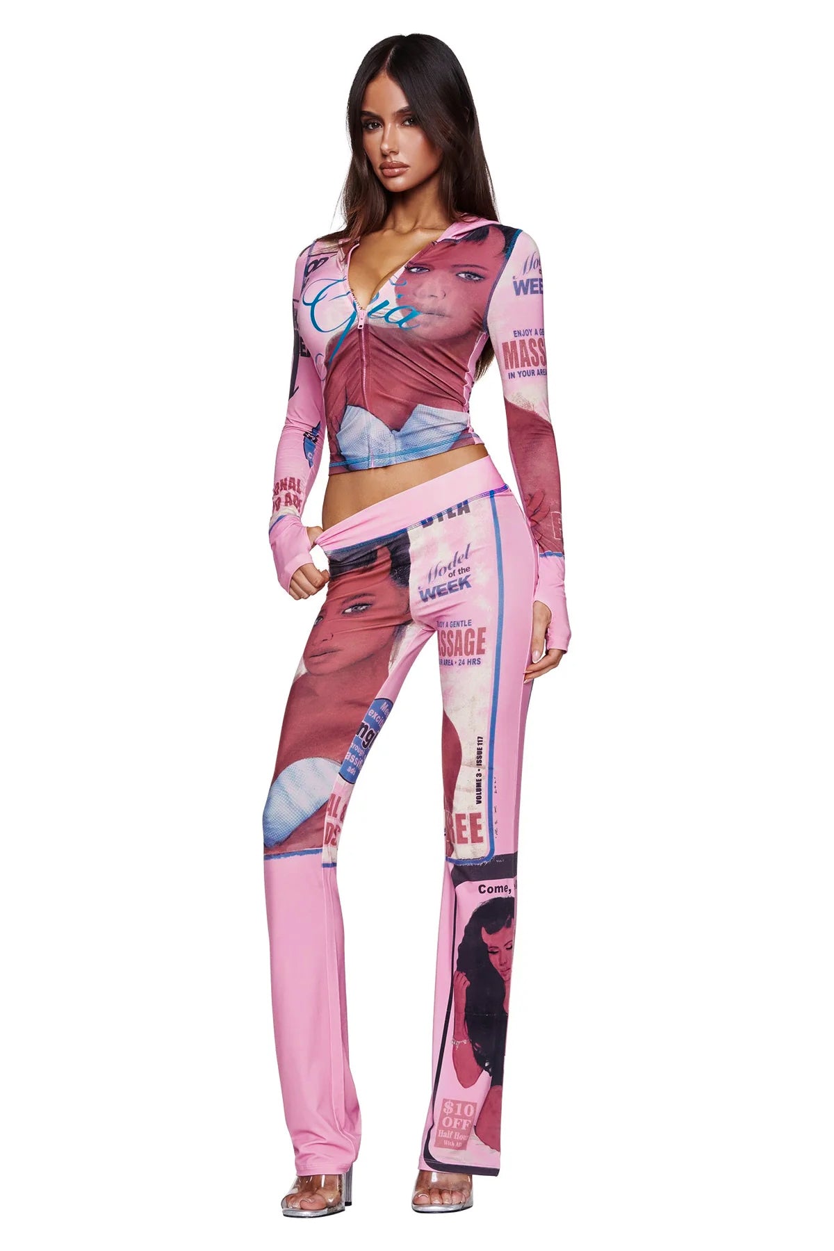 A woman wearing the I.AM.GIA T-REX BLARE HOODIE in pink, a fitted bamboo-fabrication piece featuring bold magazine and newspaper graphic prints with faces and striking text, stands in clear heels against a white background.