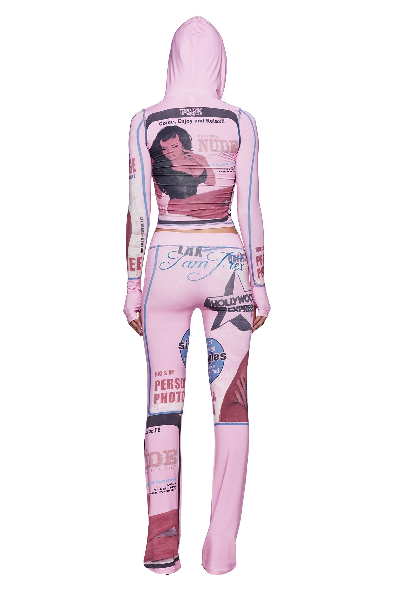 A person wearing the I.AM.GIA T-REX BLARE TRACKPANT - PINK, which features vintage magazine-inspired graphics and text, stands with their back to the camera to highlight the bold pink T-REX print design, echoing the playful aesthetic of these women’s lounge pants.