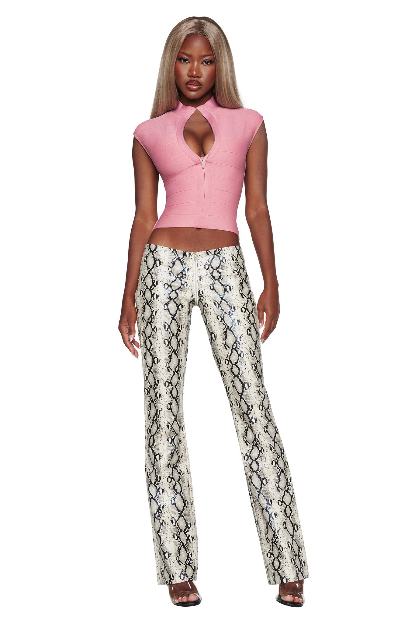 A woman stands wearing a pink, short-sleeved, zip-up top with a keyhole cutout and the HENDRIX 2.0 PANT - CREAM SNAKE by I.AM.GIA — high-waisted, straight leg pants in white faux python leather. Sporting long, straight blonde hair and black heels, she makes these I.AM.GIA statement pants the highlight of her evening ensemble.