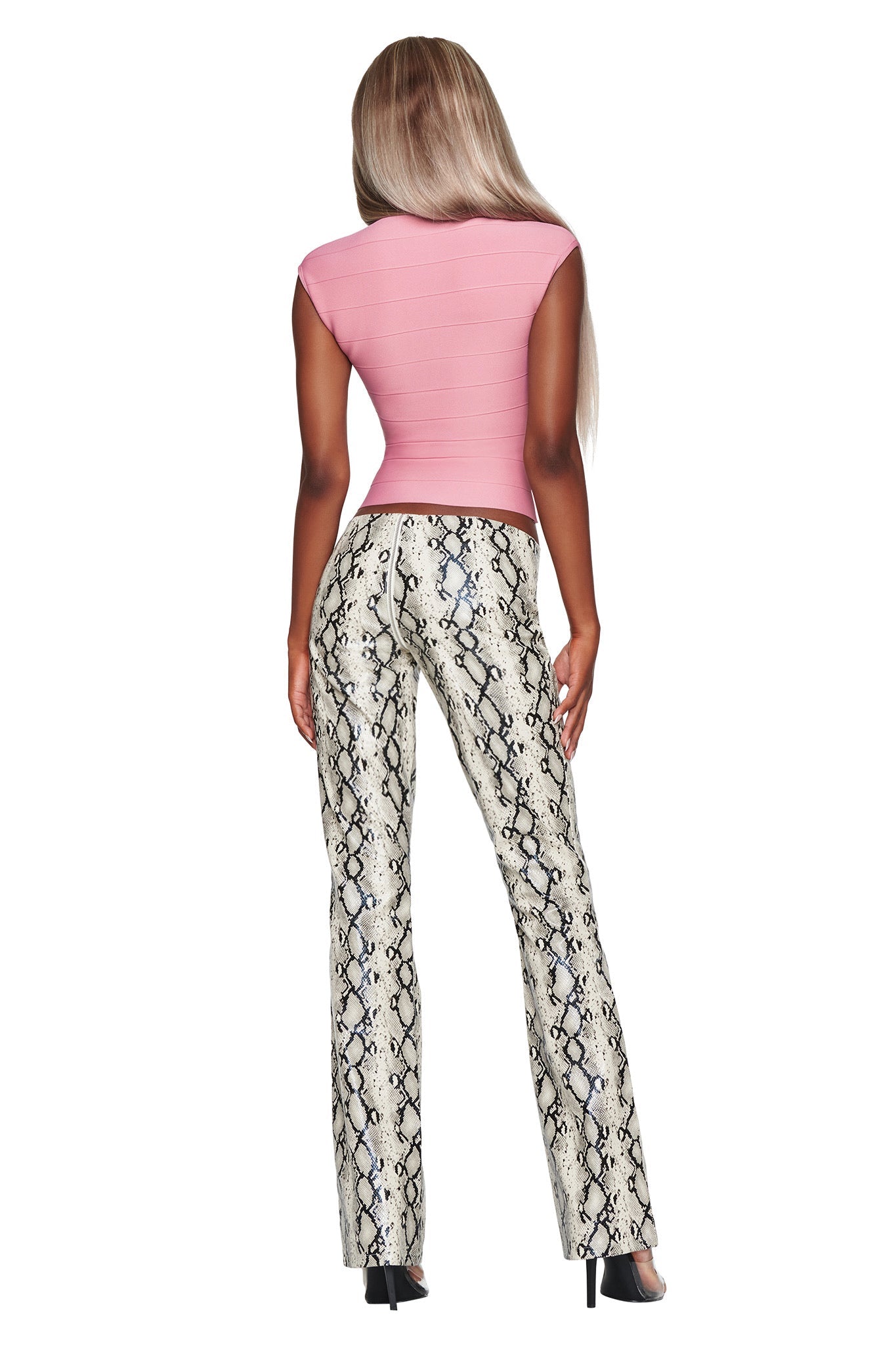 A woman with long, light brown hair is shown from the back against a white background, wearing a pink fitted top, black heels, and the I.AM.GIA HENDRIX 2.0 PANT in Cream Snake—high-waisted faux python leather pants featuring a straight leg cut.