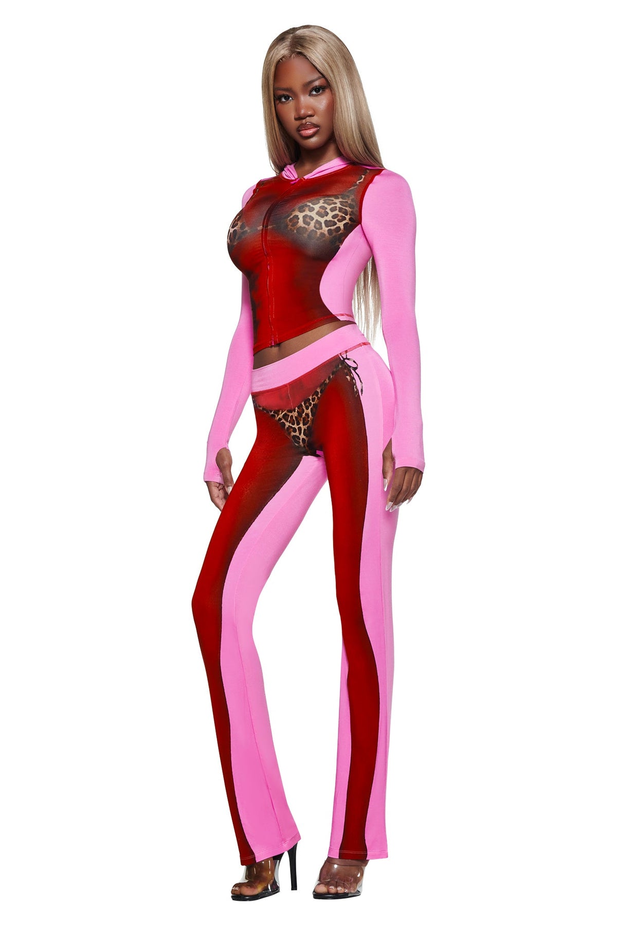 A woman in the I.AM.GIA T-REX SPRAY BODY BLARE HOODIE - PINK, with bold prints and waist cutouts, poses in black heels against a white background.