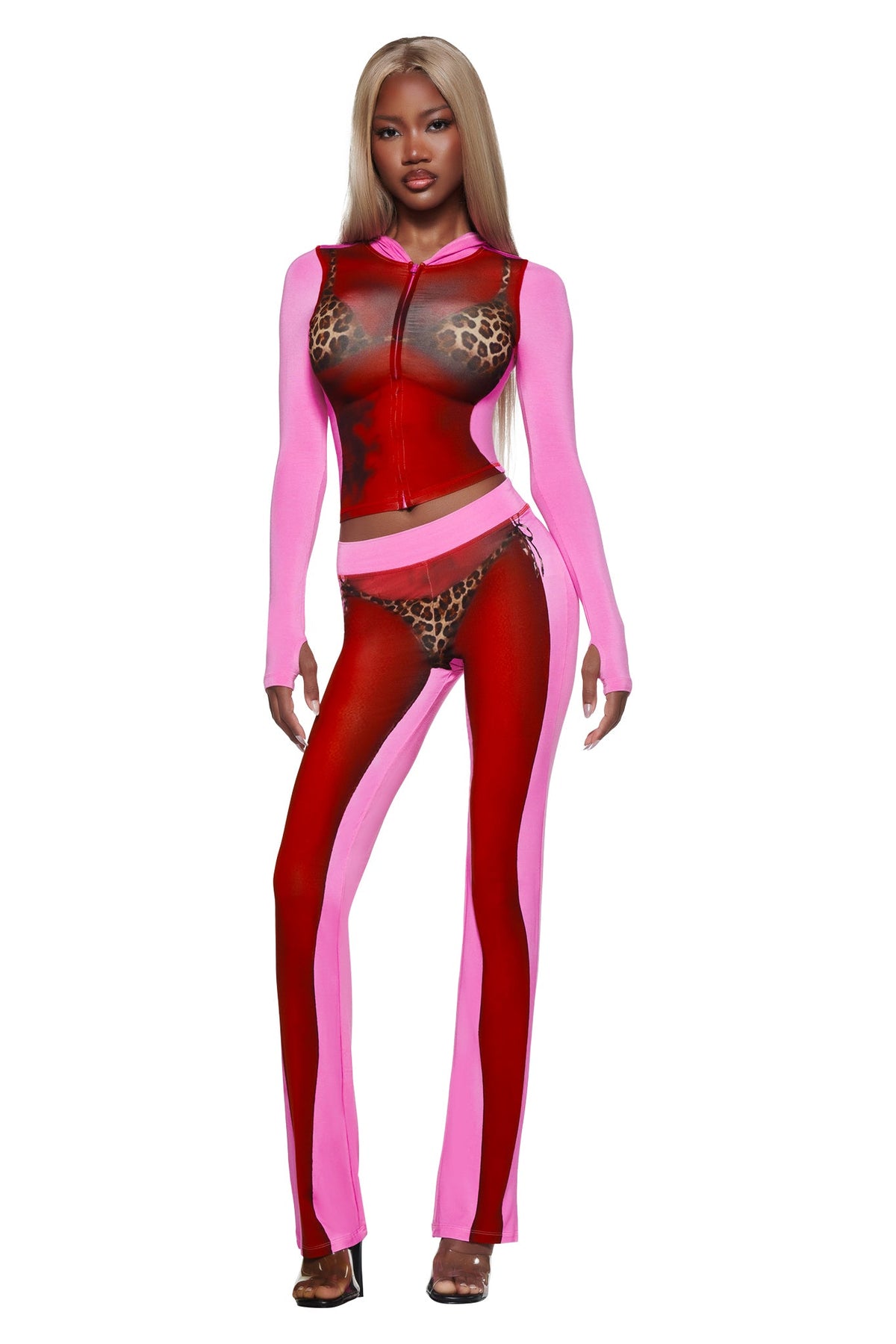 A woman wears the T-REX SPRAY BODY BLARE HOODIE - PINK by I.AM.GIA, featuring sheer pink fabric and bold prints, confidently posing in heels against a white background.