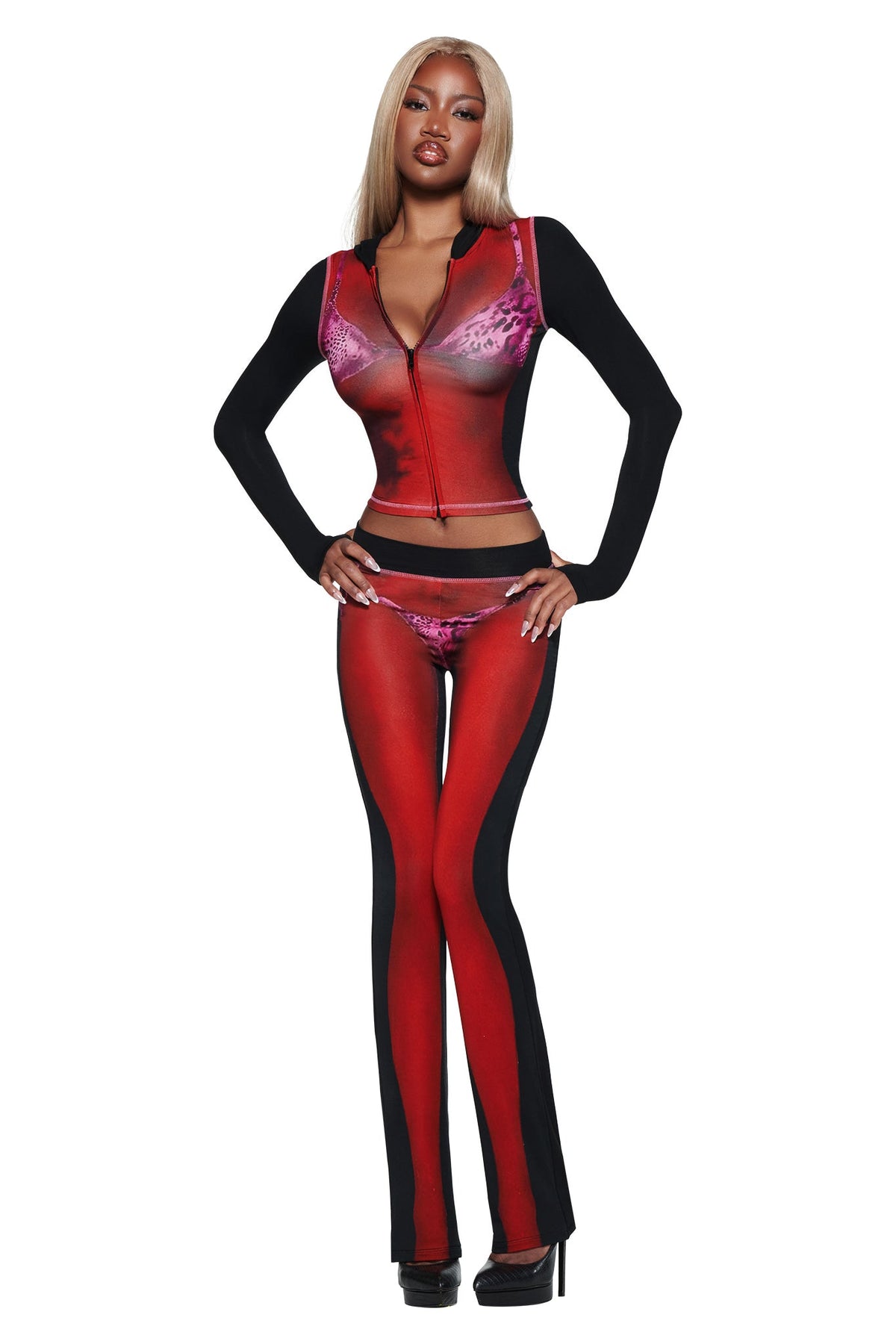 A woman with long blonde hair poses confidently in I.AM.GIA’s T-REX SPRAY BODY BLARE TRACKPANT - BLACK, paired with black heels, perfect for airport style against a white background.