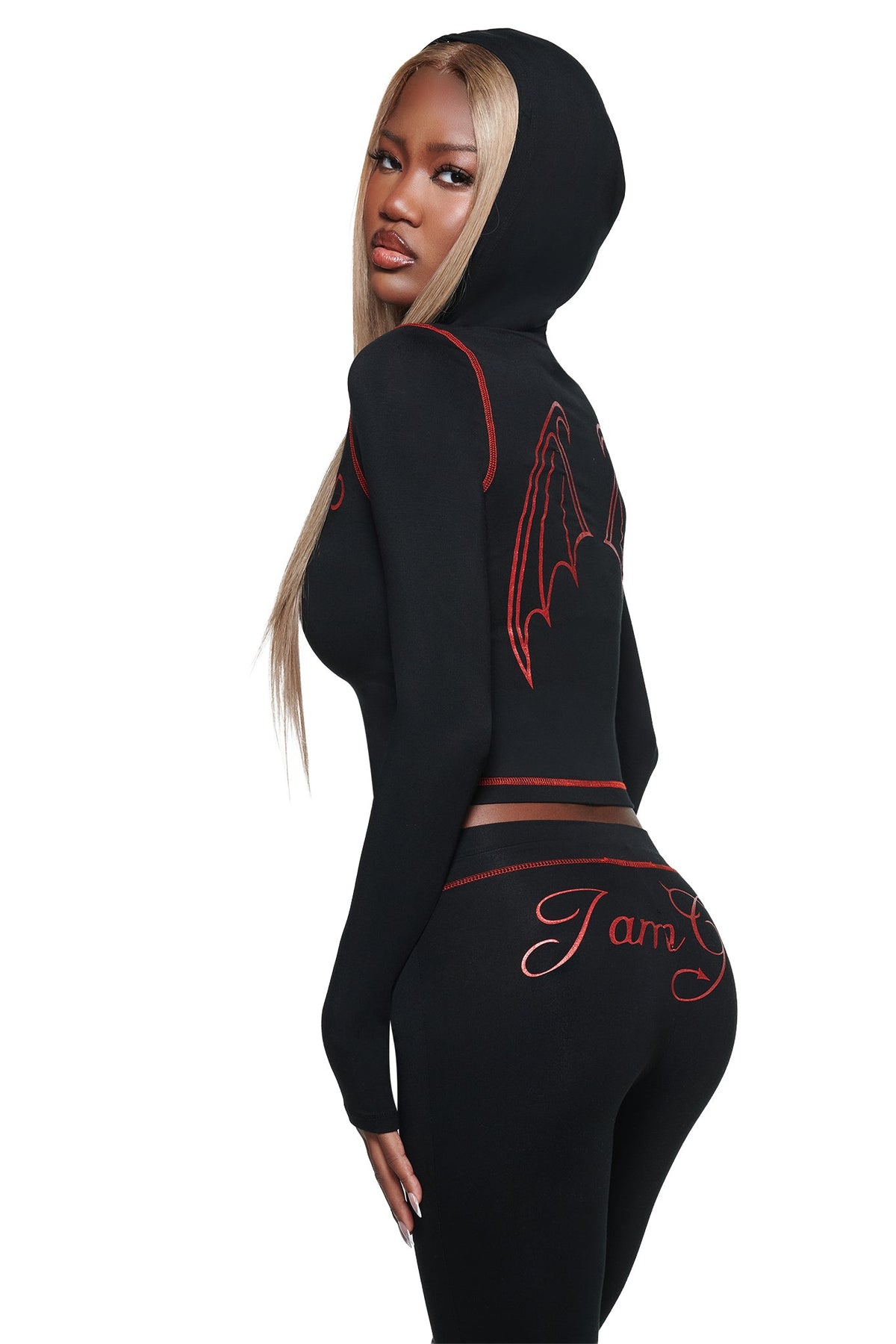 A woman poses looking over her shoulder against a white background, showcasing the I.AM.GIA BLARE FUR TRIM HOODIE in black, a fitted hoodie with red stitching and a striking bat-wing design on the back.