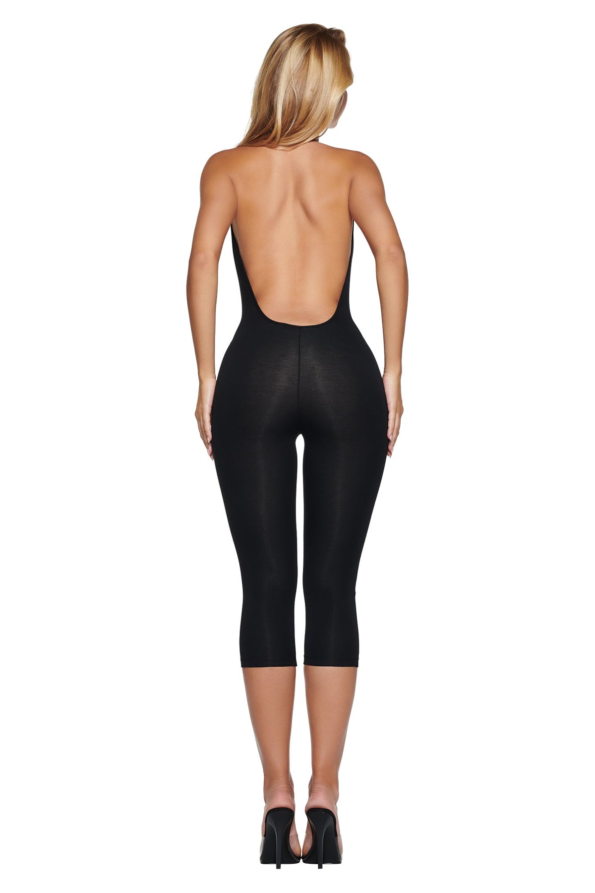 Back view of a person wearing a black BLARE HALTER CAPRI JUMPSUIT and black high-heeled sandals.