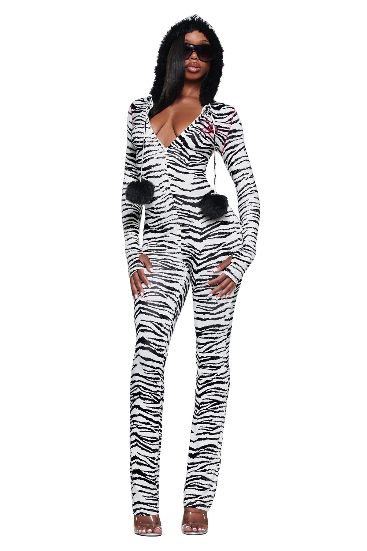 A person wearing an I.AM.GIA YVL BLARE FUR LINED JUMPSUIT - ZEBRA, featuring a long-sleeved zebra print design with a fur-lined hood and dangling black pom-poms.