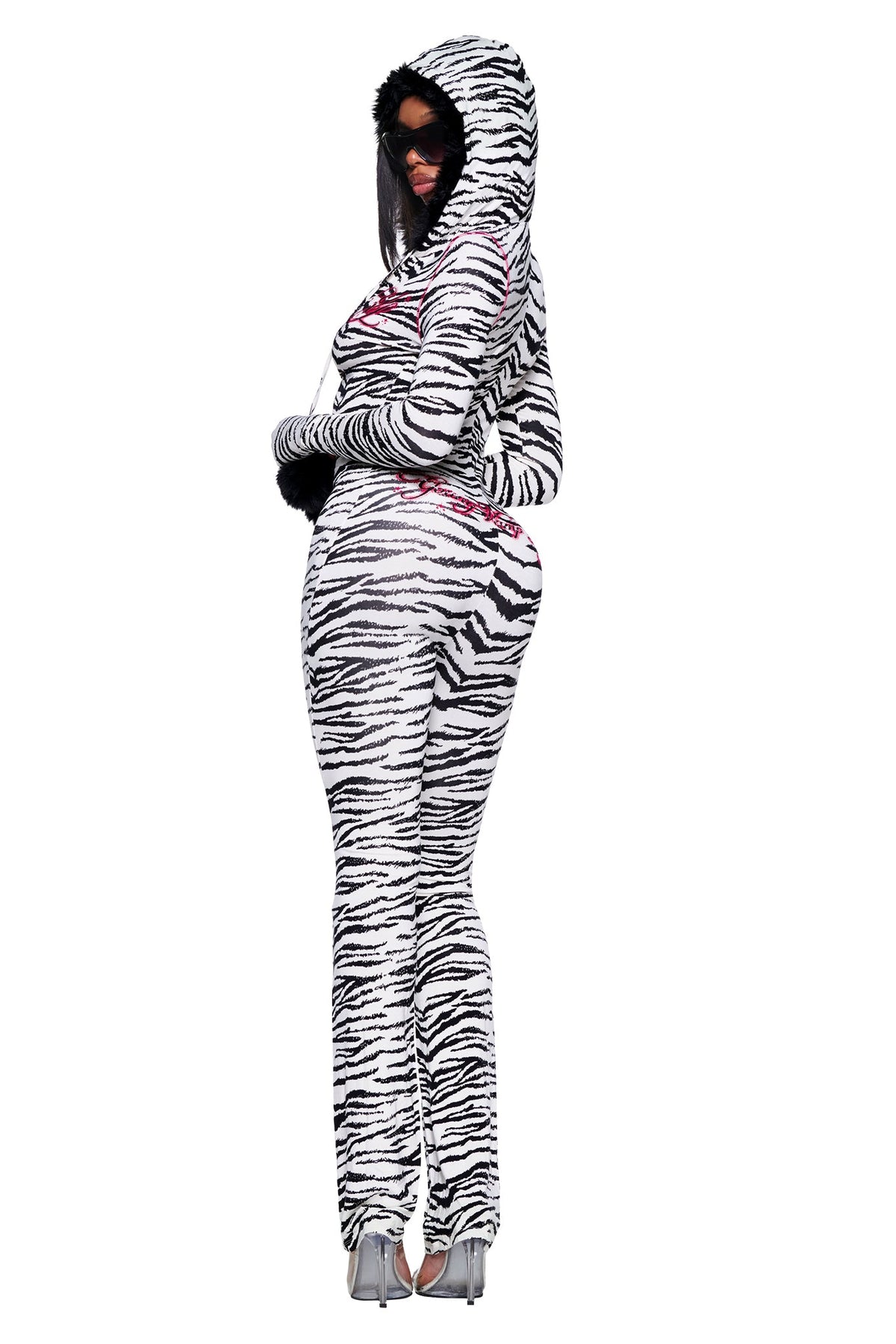 A model wearing the YVL BLARE FUR LINED JUMPSUIT - ZEBRA, a long-sleeved, zebra-print design featuring a hood and cuffs finished with black faux fur trim.