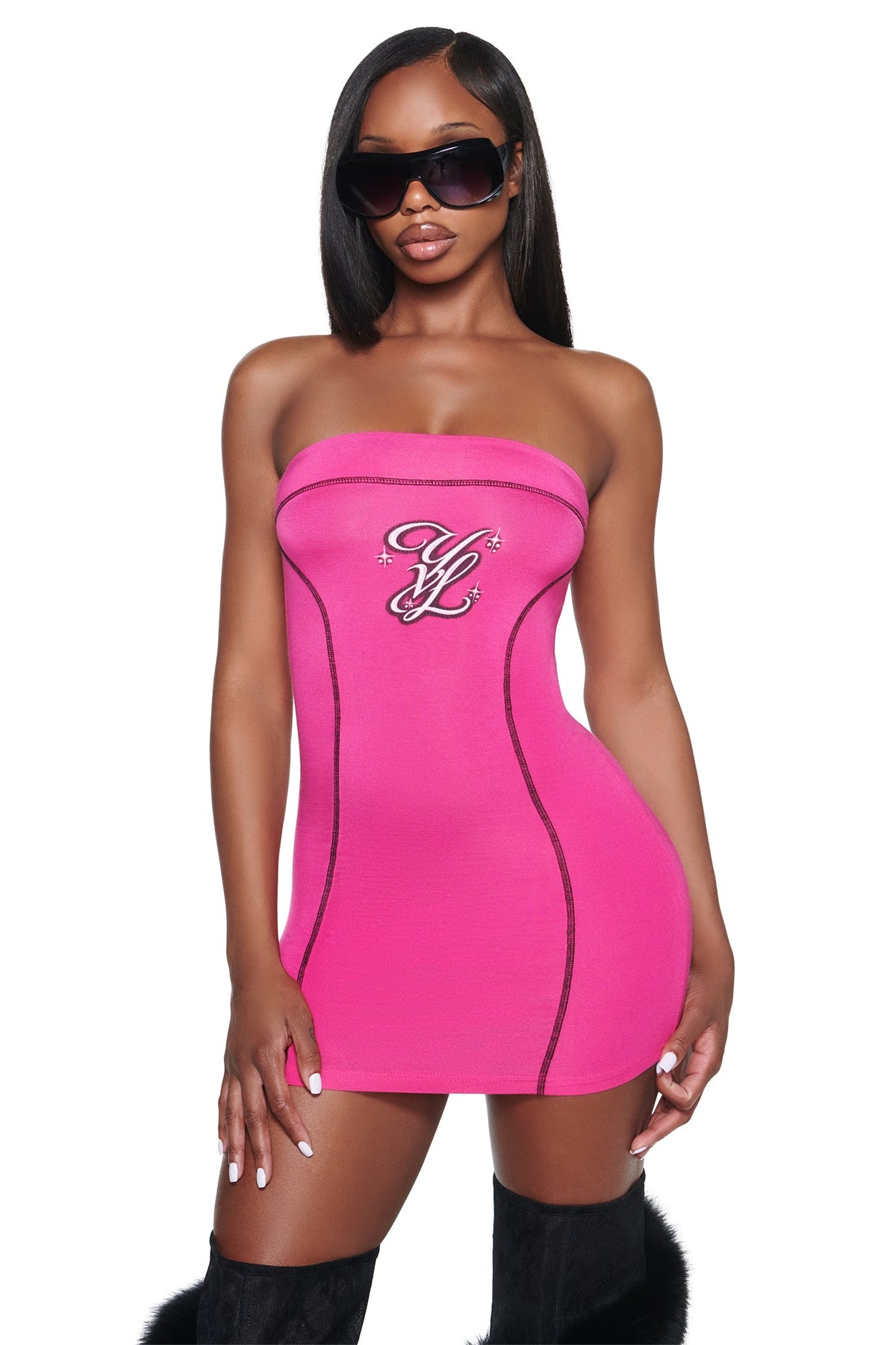 A woman wears a hot pink I.AM.GIA YVL BLARE TUBE MINI DRESS, a form-fitting strapless mini dress with black seam detailing and an embroidered logo on the chest.