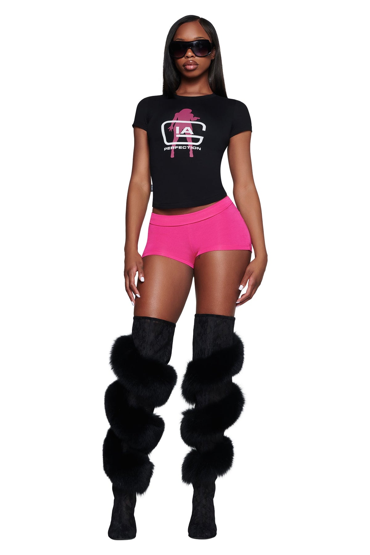 A woman wears a black YVL T-SHIRT - BLACK GIA, bright pink shorts, and black over-the-knee boots with fur trim.
