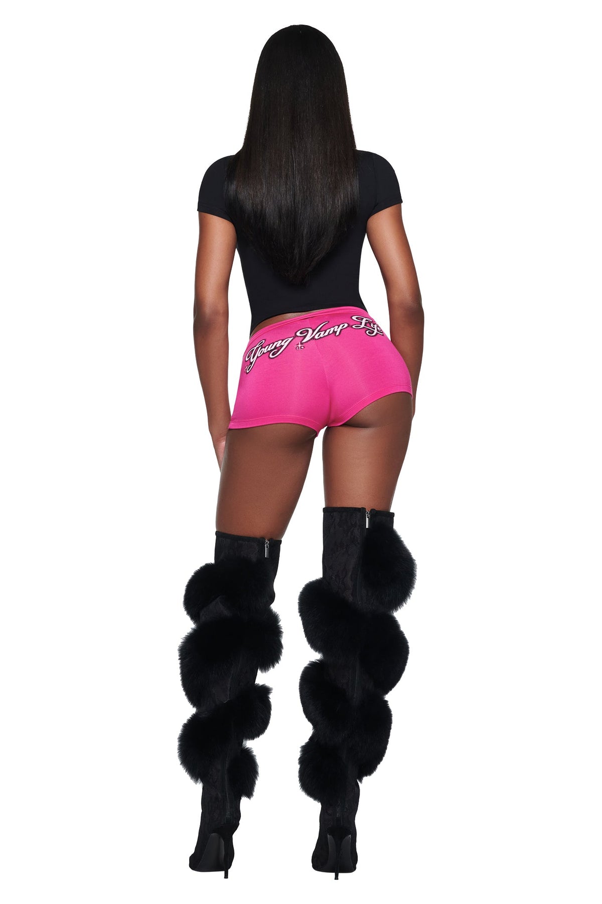 A person wearing a black YVL T-SHIRT - BLACK GIA, pink short shorts with “Young Vamp” text on the back, and black knee-high boots with fur trim.