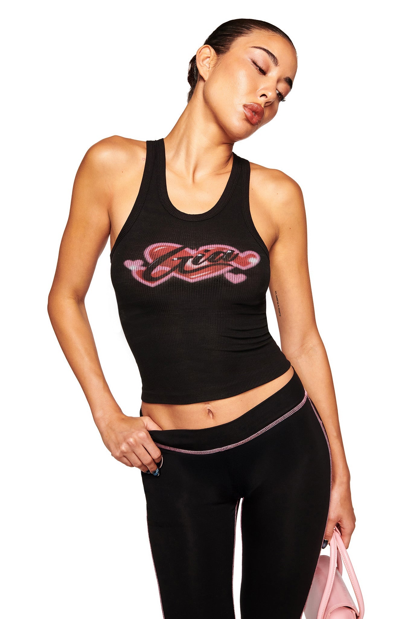 A woman wears the I.AM.GIA PENELOPE TANK - GIA AIRBRUSH, styled with black leggings featuring pink trim and a pink bag, standing against a white background with her head tilted and eyes closed.