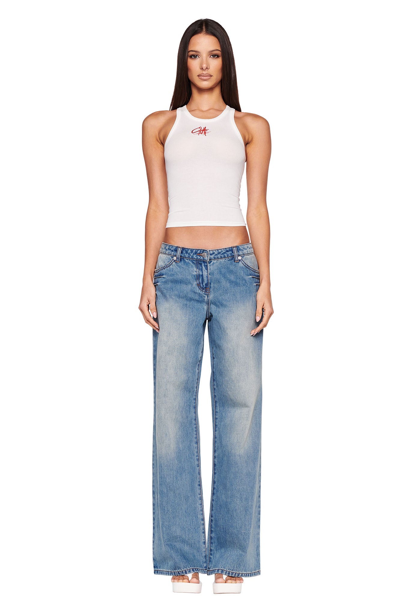 A person stands facing forward wearing a white sleeveless crop top and the DYLAN JEAN - BLUE, light blue wide-leg jeans from I.AM.GIA. Their straight hair falls past their shoulders, complementing the ensemble with light-colored platform heels against a plain white background.