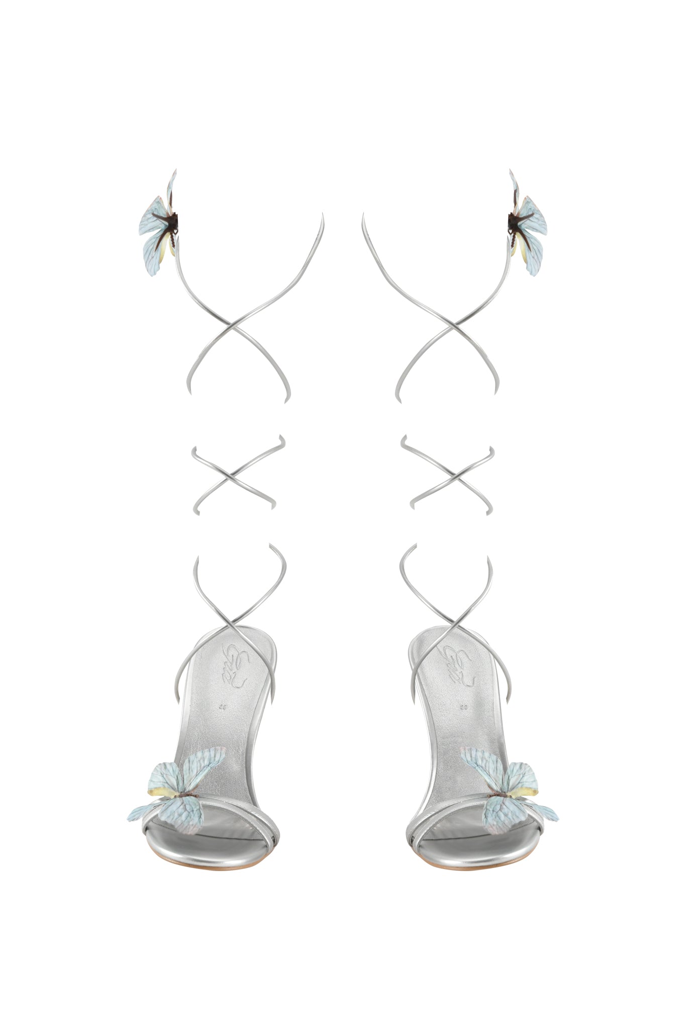 The SCARLETTE HEEL - SILVER by I.AM.GIA features elegant open toe stiletto sandals with transparent and silver strappy heels, adorned with delicate blue butterfly appliques on the toes and ankle straps, shown on a white background.