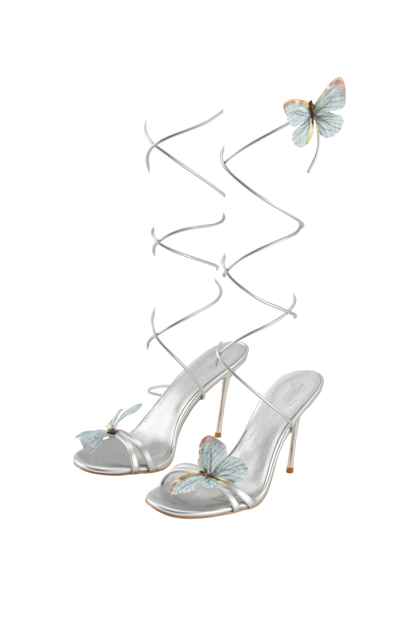 The SCARLETTE HEEL - SILVER by I.AM.GIA is a metallic strappy stiletto sandal with spiral ankle straps, open toe, and delicate light blue butterfly appliques on the toe, strap, and near the top of each spiral.