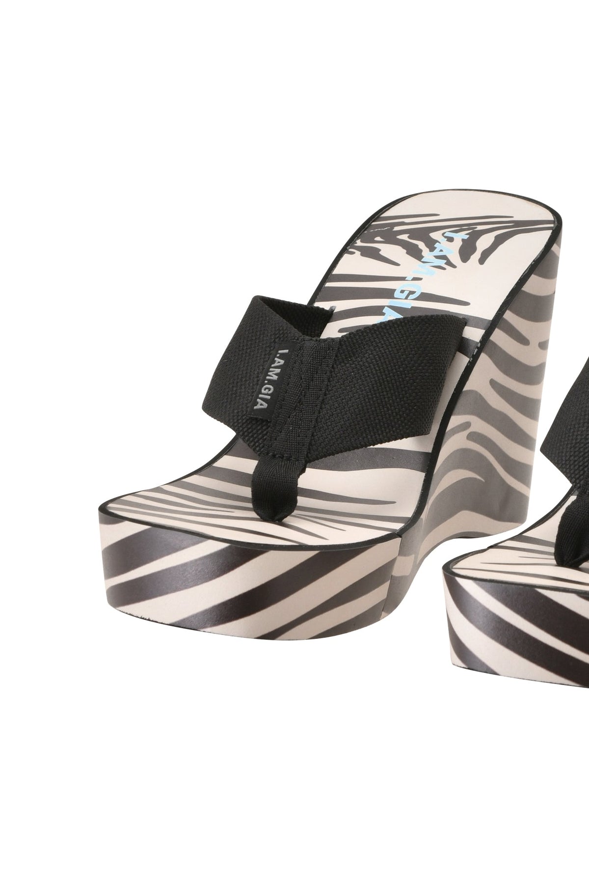 Introducing the SHELBY FLIP FLOP - FINE LINE ZEBRA by I.AM.GIA: a casual thong sandal with a bold black-and-white zebra stripe pattern on the platform and sole, complemented by a black fabric strap. The pair includes a matching sandal, partially visible on the right.