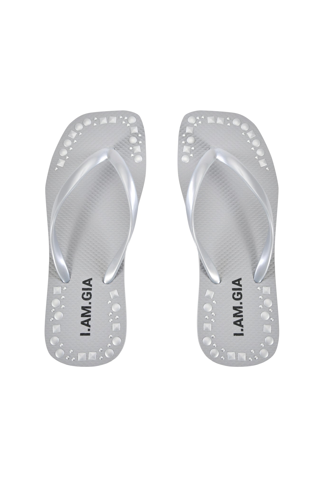 The INKA STUDDED FLIP FLOP in silver by I.AM.GIA features cut-out circle details, a comfy footbed, and “I.AM.GIA” printed in black on the insoles, displayed against a white background.