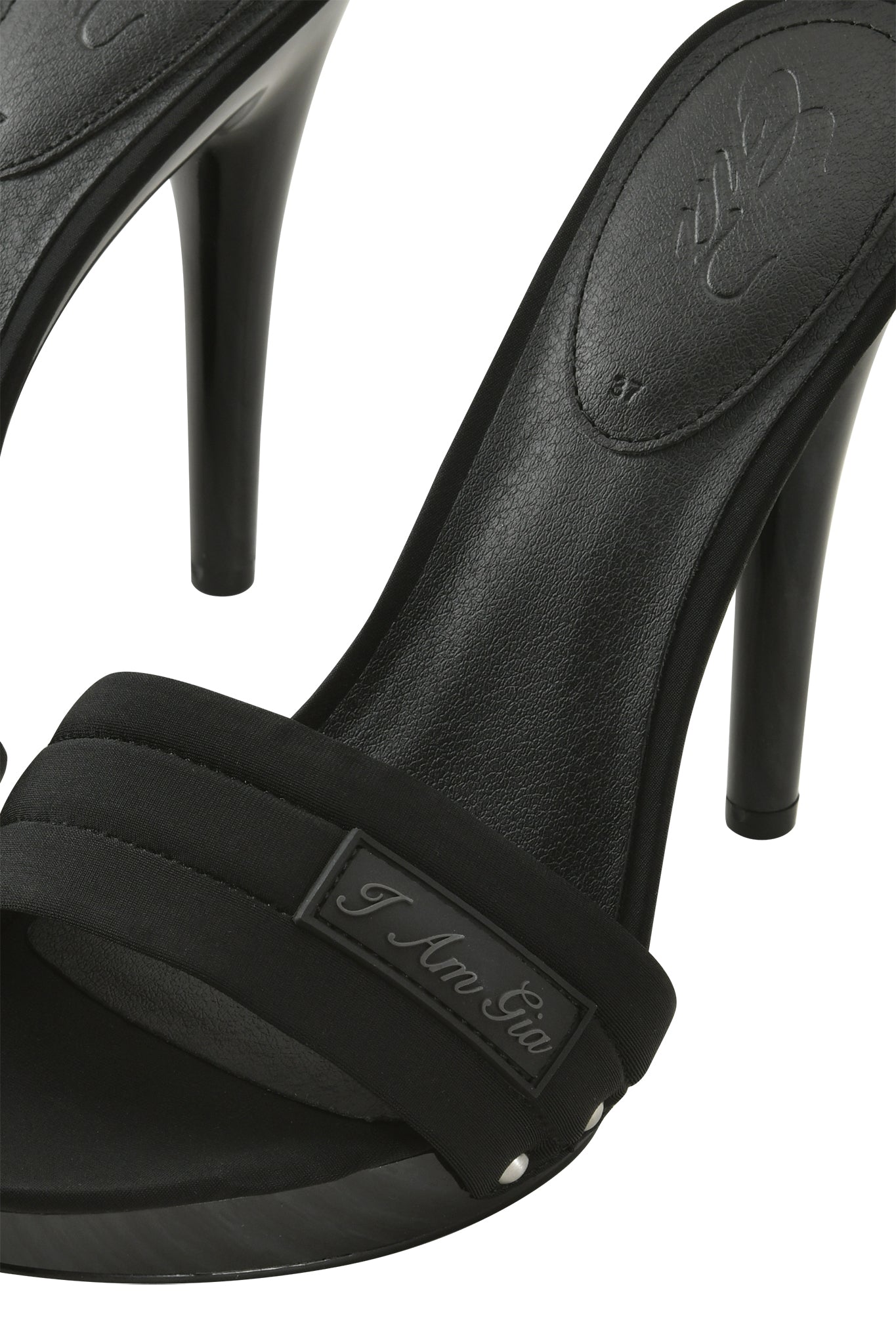 Close-up of the I.AM.GIA NICKY HEEL - BLACK NEOPRENE: black high-heeled sandals with a padded vamp strap, slip-on mule design, sleek stiletto heel, and a small metal plaque engraved with "I.AM.GIA.