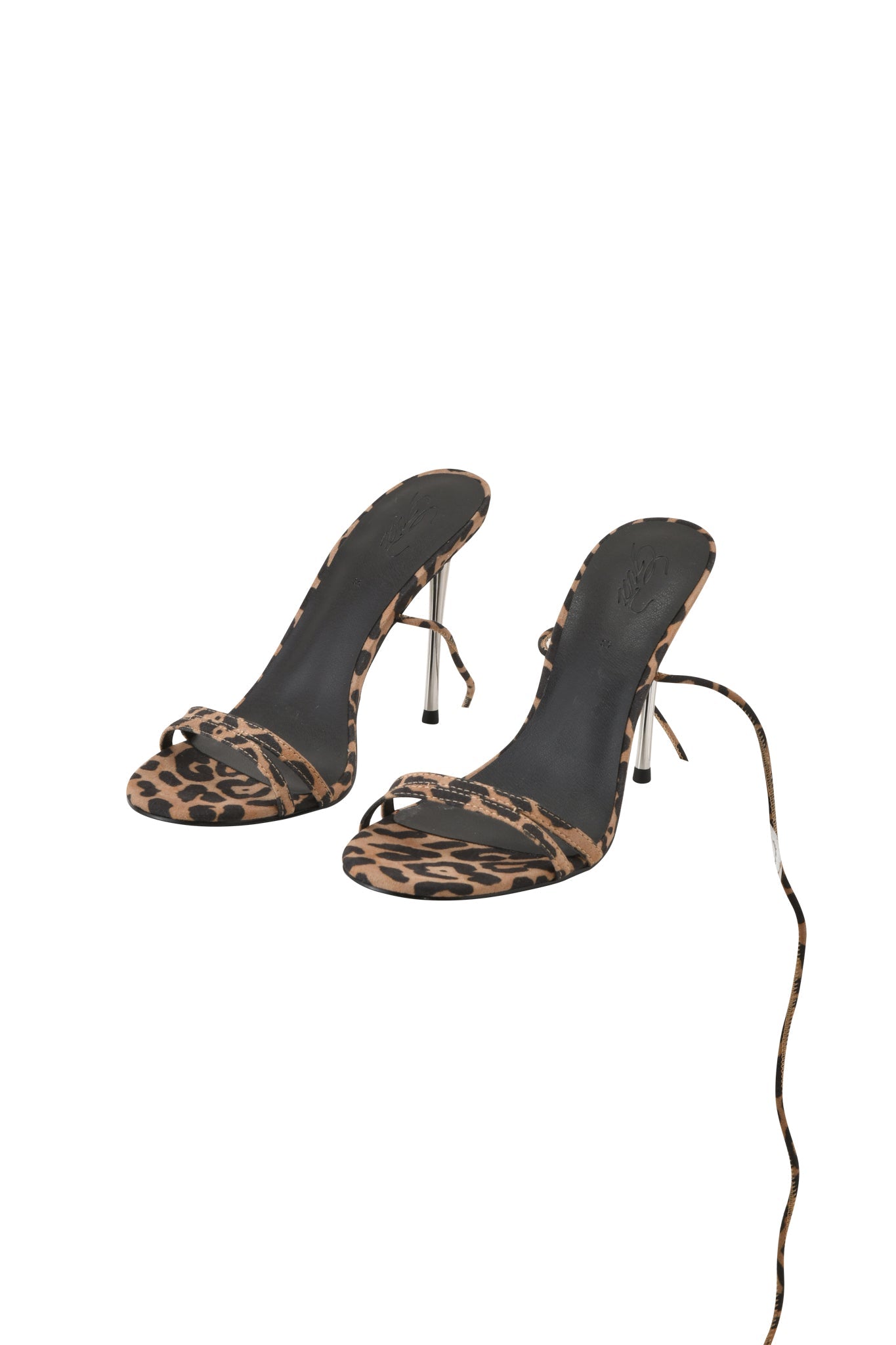 The I.AM.GIA SCARLETTE HEEL - LEOPARD features open toes, thin metal stiletto heels, black soles, leopard print strappy design, and a long strap on one shoe. Displayed on a white background.