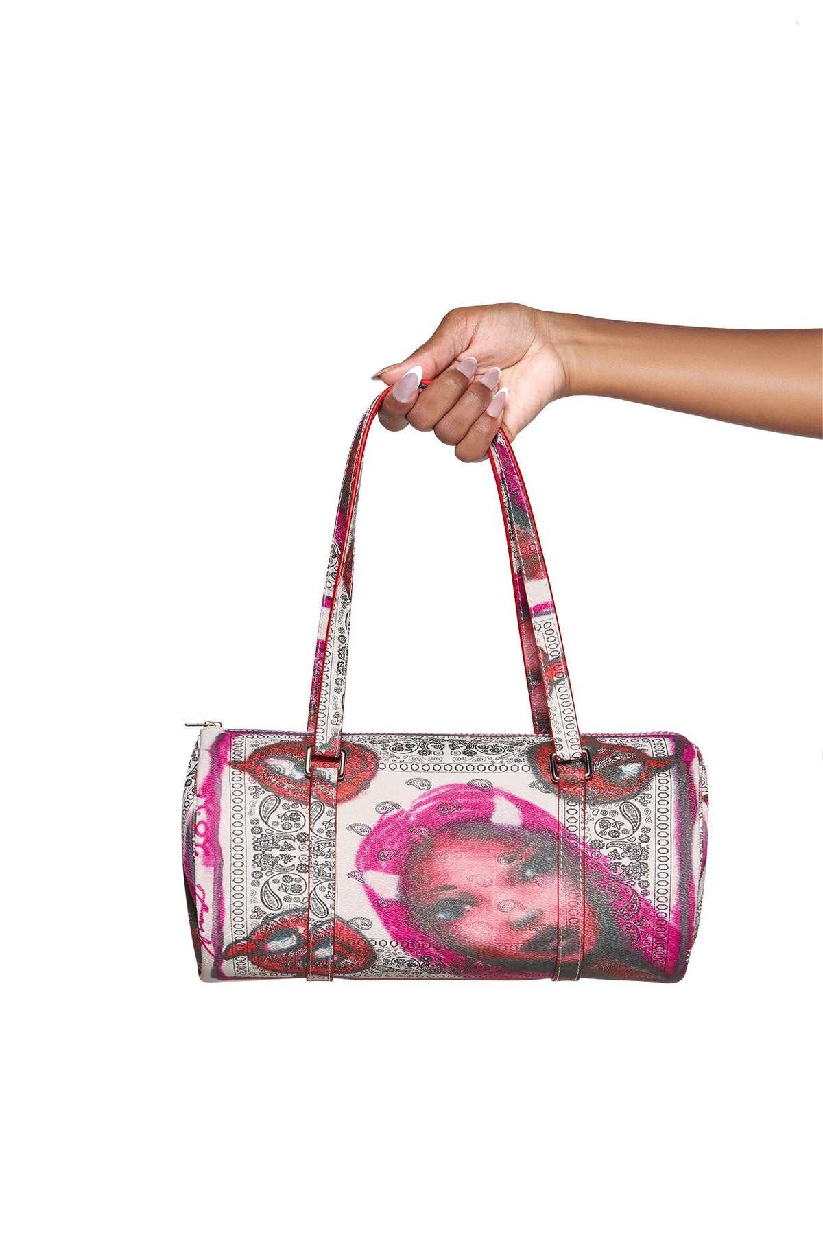 A hand with long nails holds the I.AM.GIA T-REX BARREL BAG - PAISLEY FACE, a faux leather purse featuring two straps and vibrant pink, red, and gray paisley face art on white.