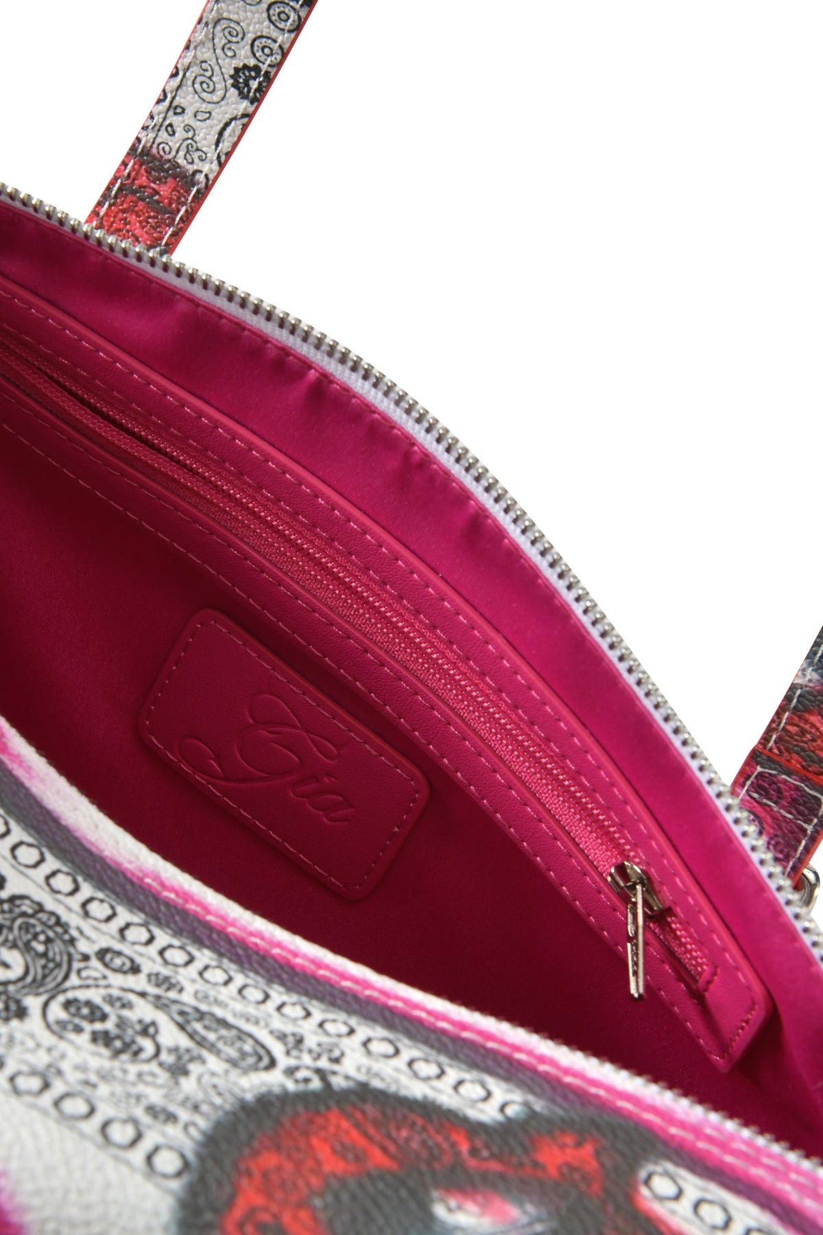 Close-up of the T-REX BARREL BAG - PAISLEY FACE by I.AM.GIA showing a pink interior with a zip pocket, stitched label, and patterned faux leather in red, black, and white on the outer edge.