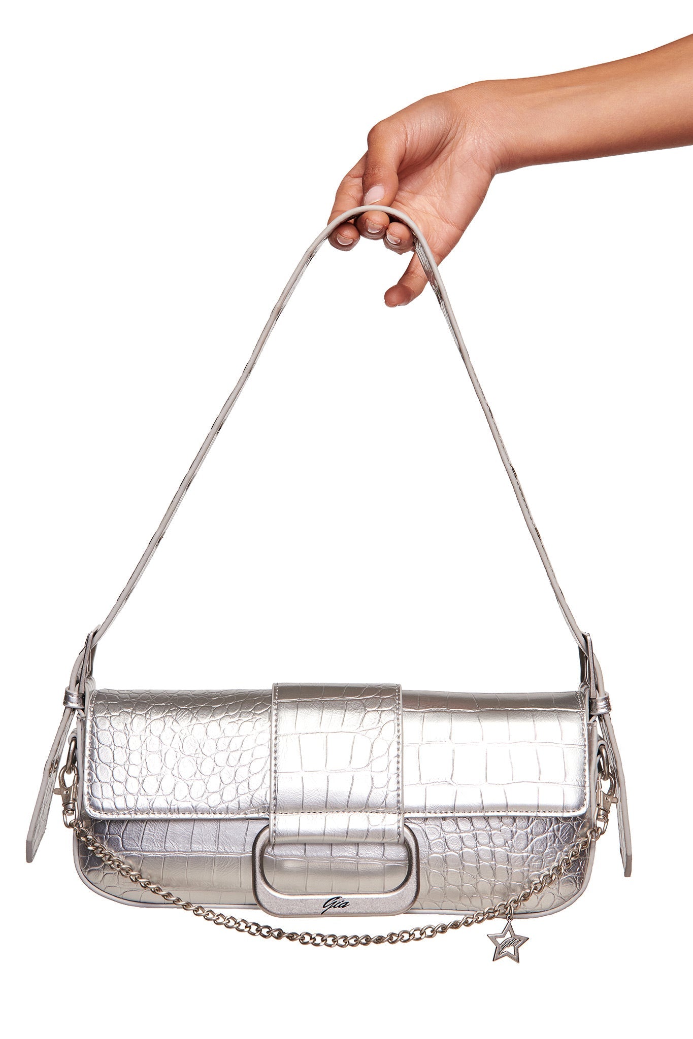 A hand holds the I.AM.GIA MILA METALLIC BAG in silver metallic with faux crocodile texture, chain strap, star charm, and subtle branding, set against a white background.