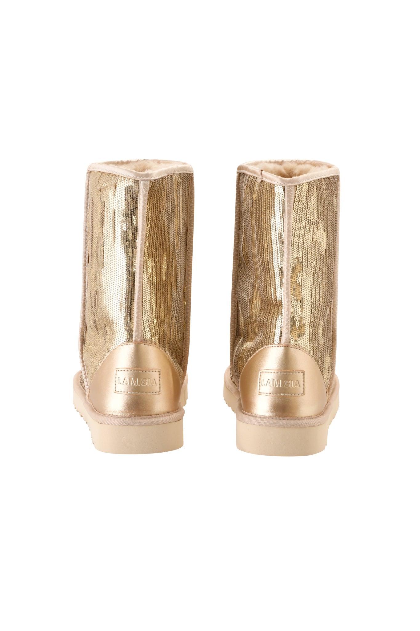 A pair of ELVIRA SEQUIN BOOT - GOLD by I.AM.GIA, featuring shimmering gold sequins and cream-colored soles, shown from the back. These mid-calf boots display a label on the heel reading “I.AM.GIA” and reveal a soft faux fur lining at the top.