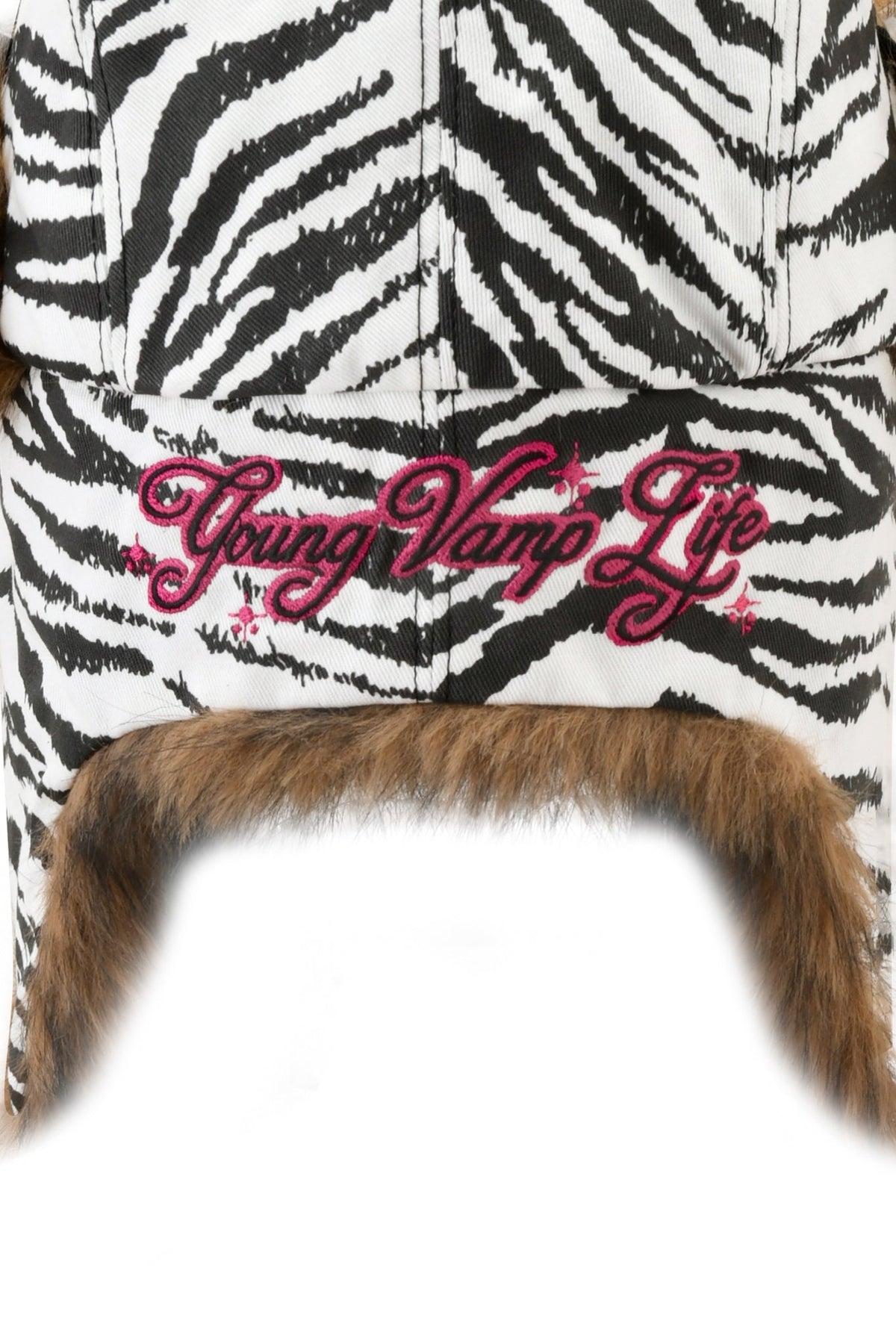 I.AM.GIA YVL FUR TRAPPER HAT - ZEBRA in zebra-print canvas with brown faux fur trim and “Young Vamp Life” embroidered in pink on the back.