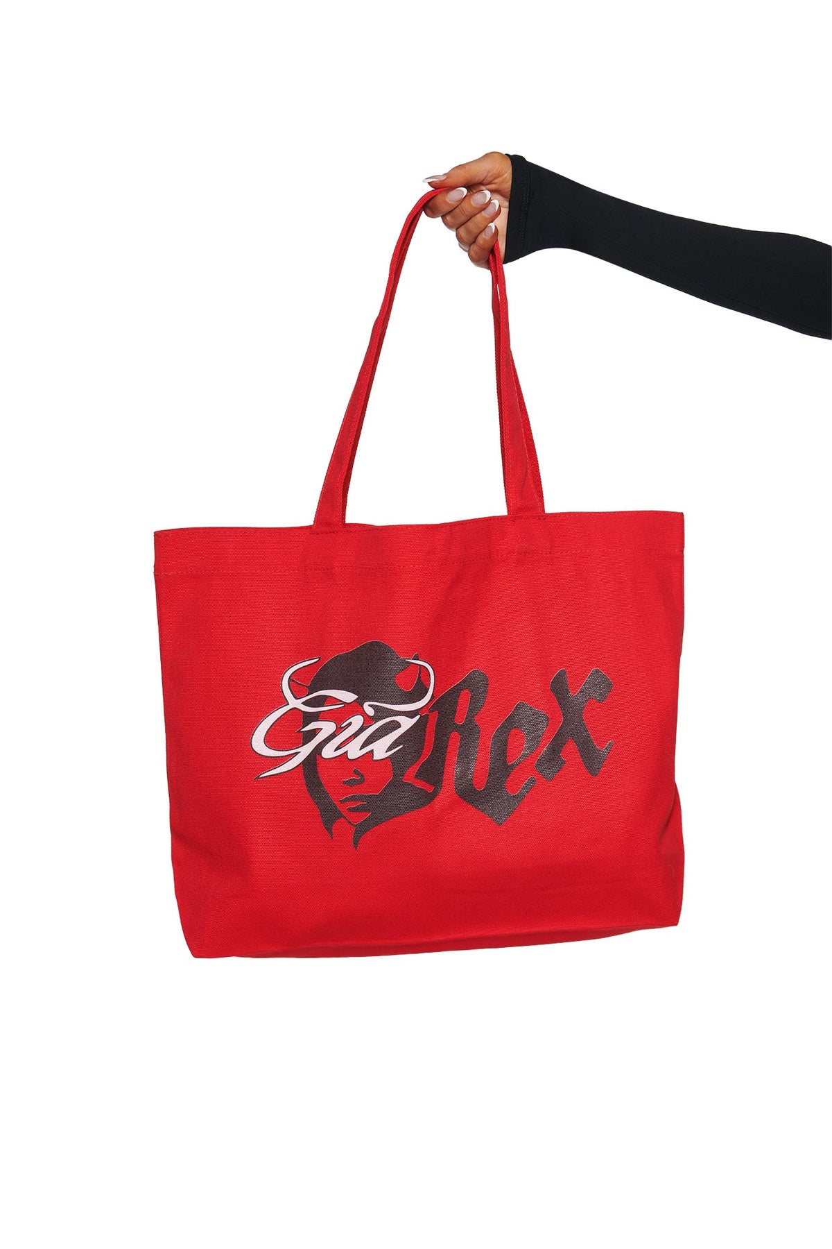 A hand holds the T-REX TOTE BAG - RED by I.AM.GIA, featuring devil girl artwork and “Bad Rex” text, creating a bold, eye-catching laptop tote against a white background.