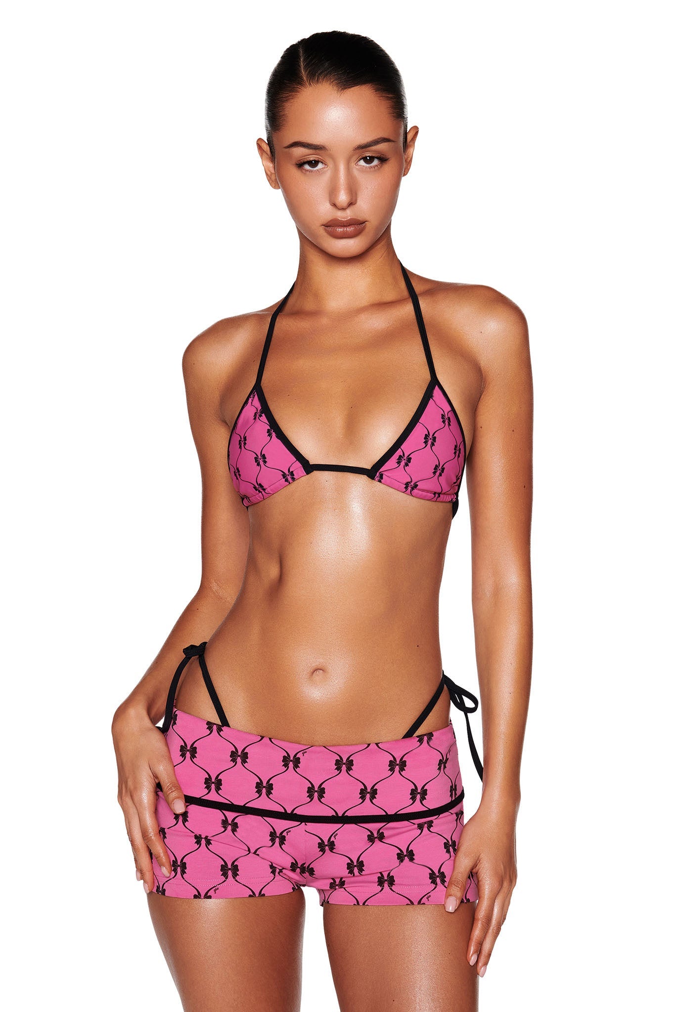 Showcasing the I.AM.GIA MONROE BIKINI TOP - PINK : DIGITAL : GIRLY POP, an individual confidently stands with a relaxed posture against a plain white background. The design features thin black straps and a playful Girly Pop print.