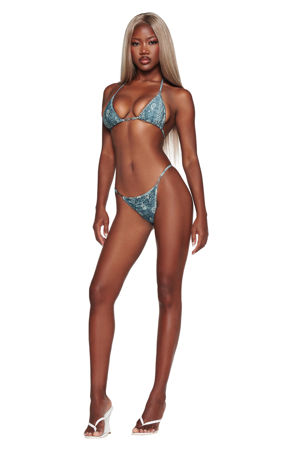 A woman with long blonde hair wearing the I.AM.GIA T-REX AVA Bikini Bottom in Blue Bandana and clear high-heeled sandals stands against a white background.