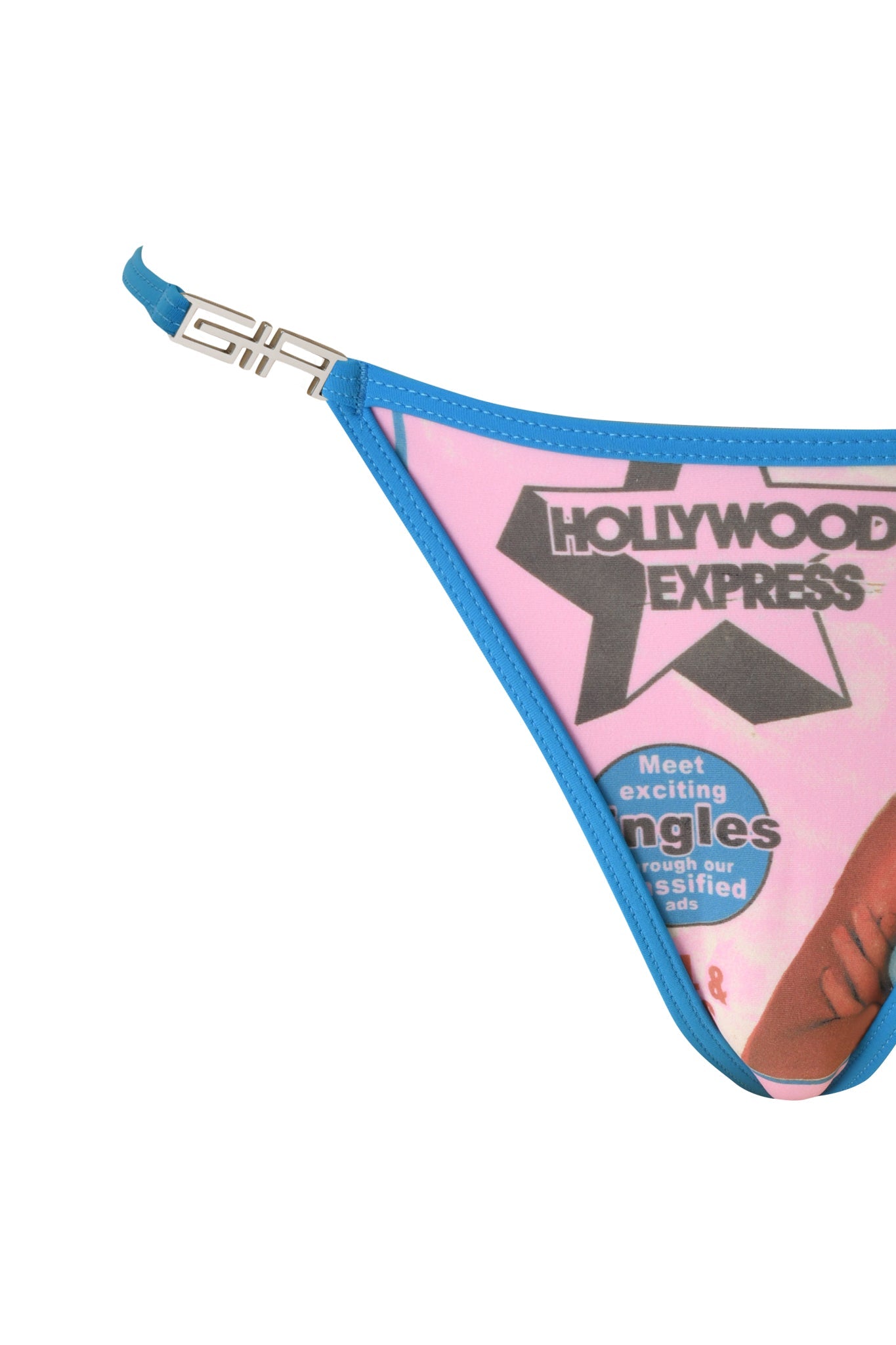 Close-up of the T-REX AVA BIKINI BOTTOM - PINK by I.AM.GIA, featuring a blue and baby pink colorway with a metal clasp detail and partial text reading "HOLLYWOOD EXPRESS" and "Meet exciting singles" printed on the fabric, capturing the playful style of this G-string bikini bottom.