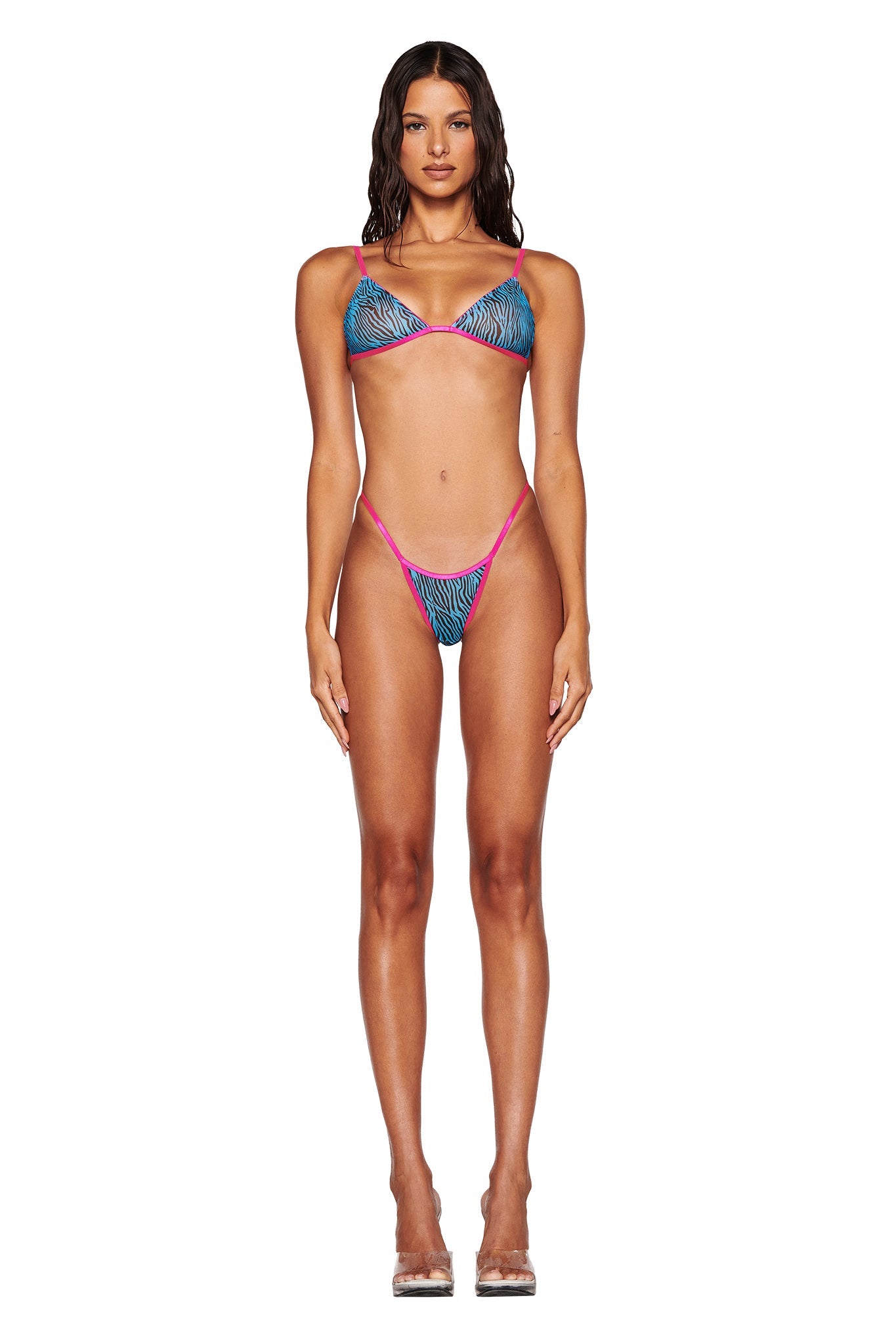 A woman stands facing forward in the I.AM.GIA LILAH SET - BLUE : ZEBRA : BLUE ZEBRA, showcasing a colorful bikini with an eye-catching blue zebra pattern. Her long, wet-look hair cascades down as she remains barefoot against a plain white background, highlighting her and the vibrant swimwear design.