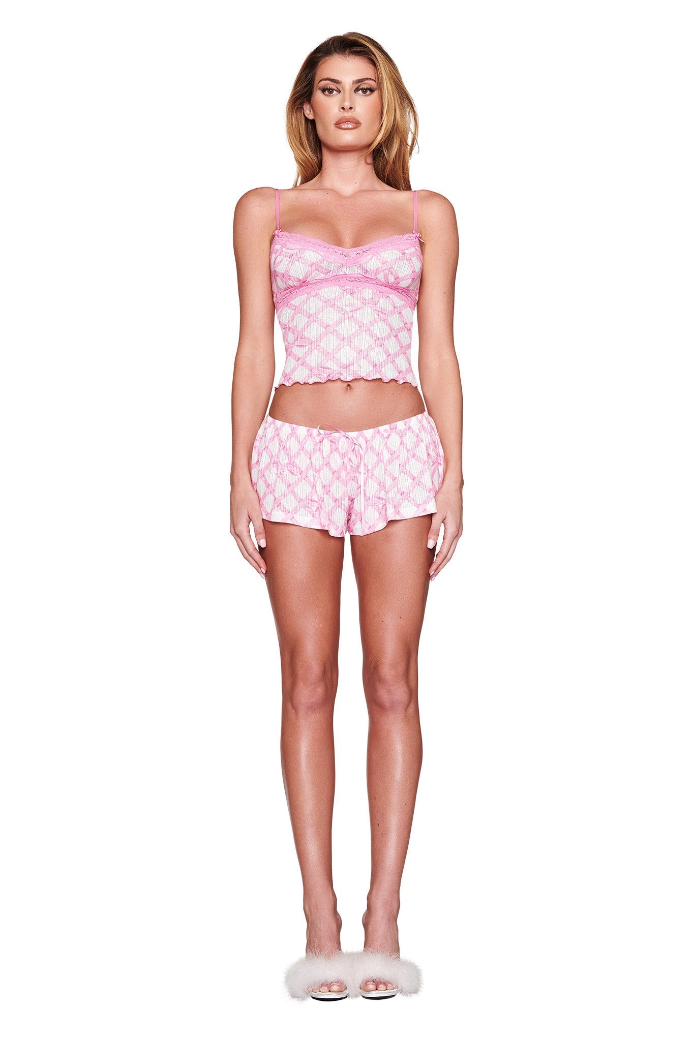 A person models the VIVIENNE SHORT - PINK set in "TIE ME UP IN GIA" print by I.AM.GIA, featuring a camisole and sleep shorts. They complete the look with white fluffy high-heeled slippers, set against a plain white backdrop.