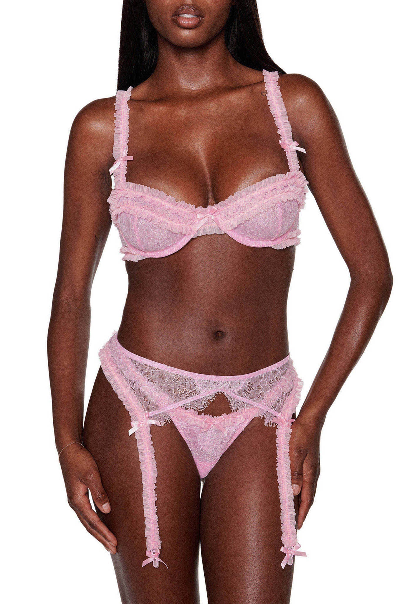 A person showcasing the MADISON 3 PIECE SET - PINK from I.AM.GIA, which includes an adjustable bra, a garter belt, and a lace thong set against a white background. The design highlights intricate lace detailing and delicate ribbon accents.