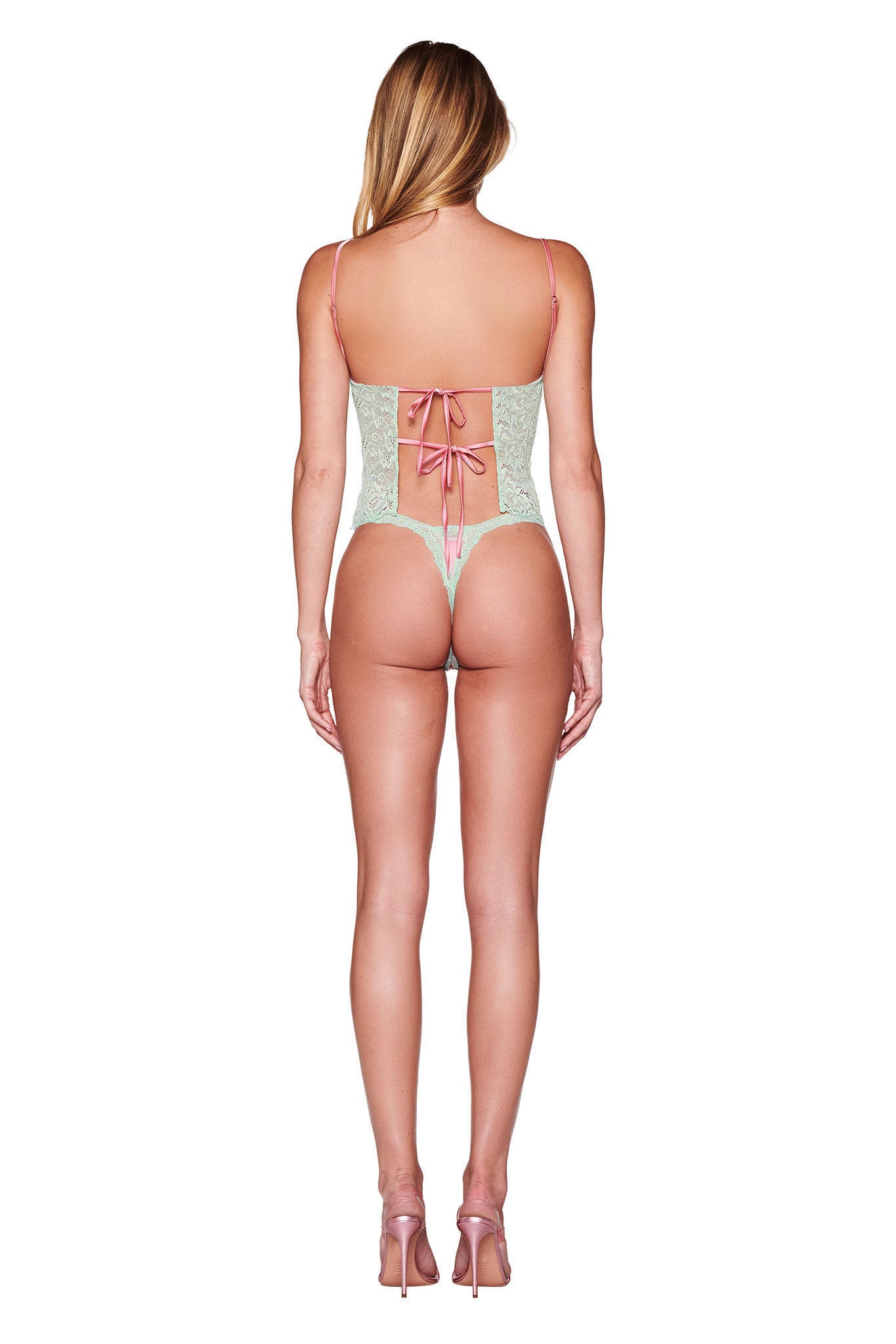 A person modeling the I.AM.GIA LOLO 2 PIECE SET in pink is elegantly depicted from the back, showcasing its sophisticated lace-up detail and delicate spaghetti straps. Complementing their look with pink high heels against a plain white backdrop, they radiate effortless sophistication.
